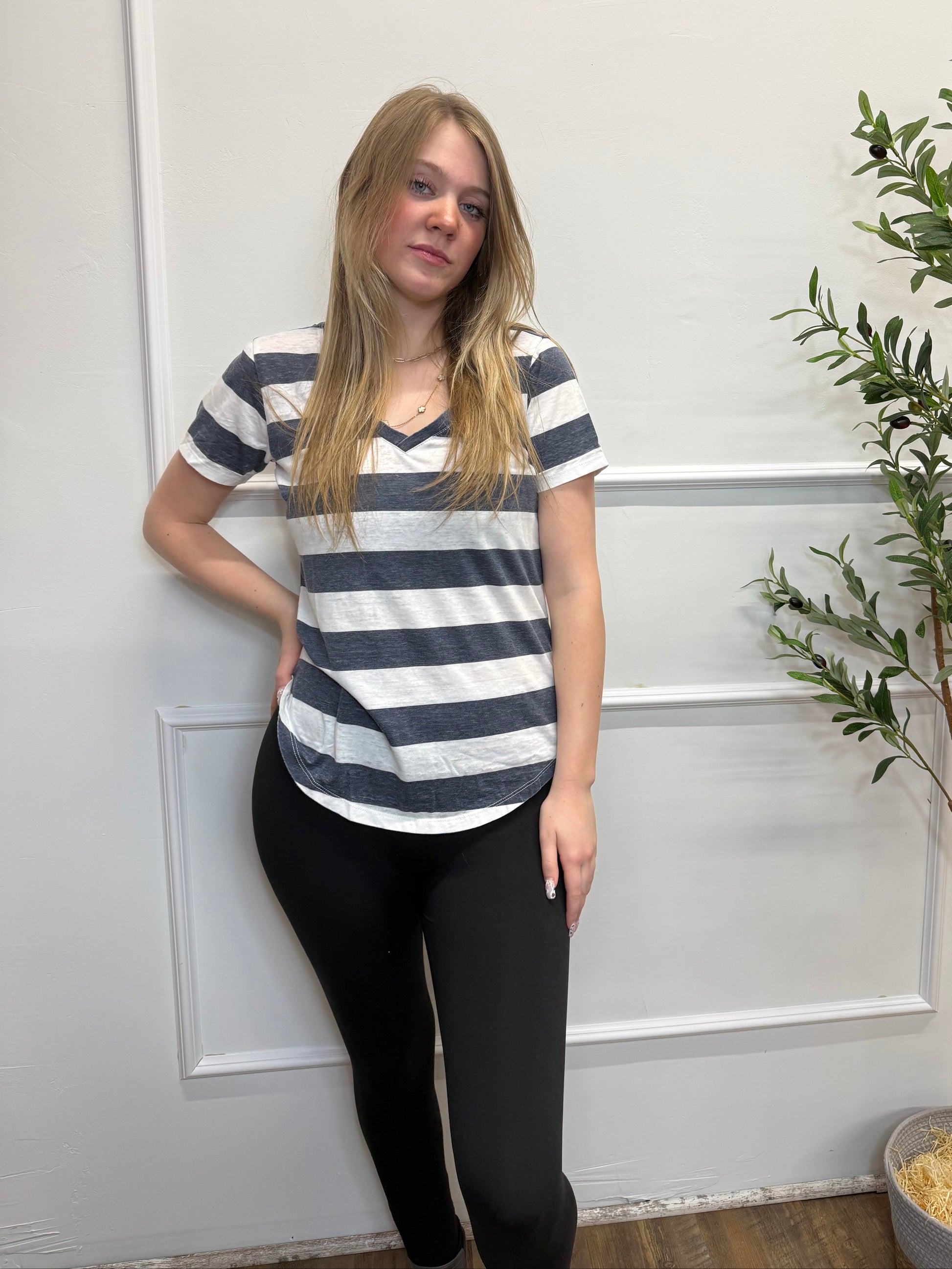 Person wearing a striped shirt and black pants standing in front of a white door with greenery.