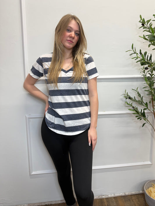 Person wearing a striped shirt and black pants standing in front of a white door with greenery.