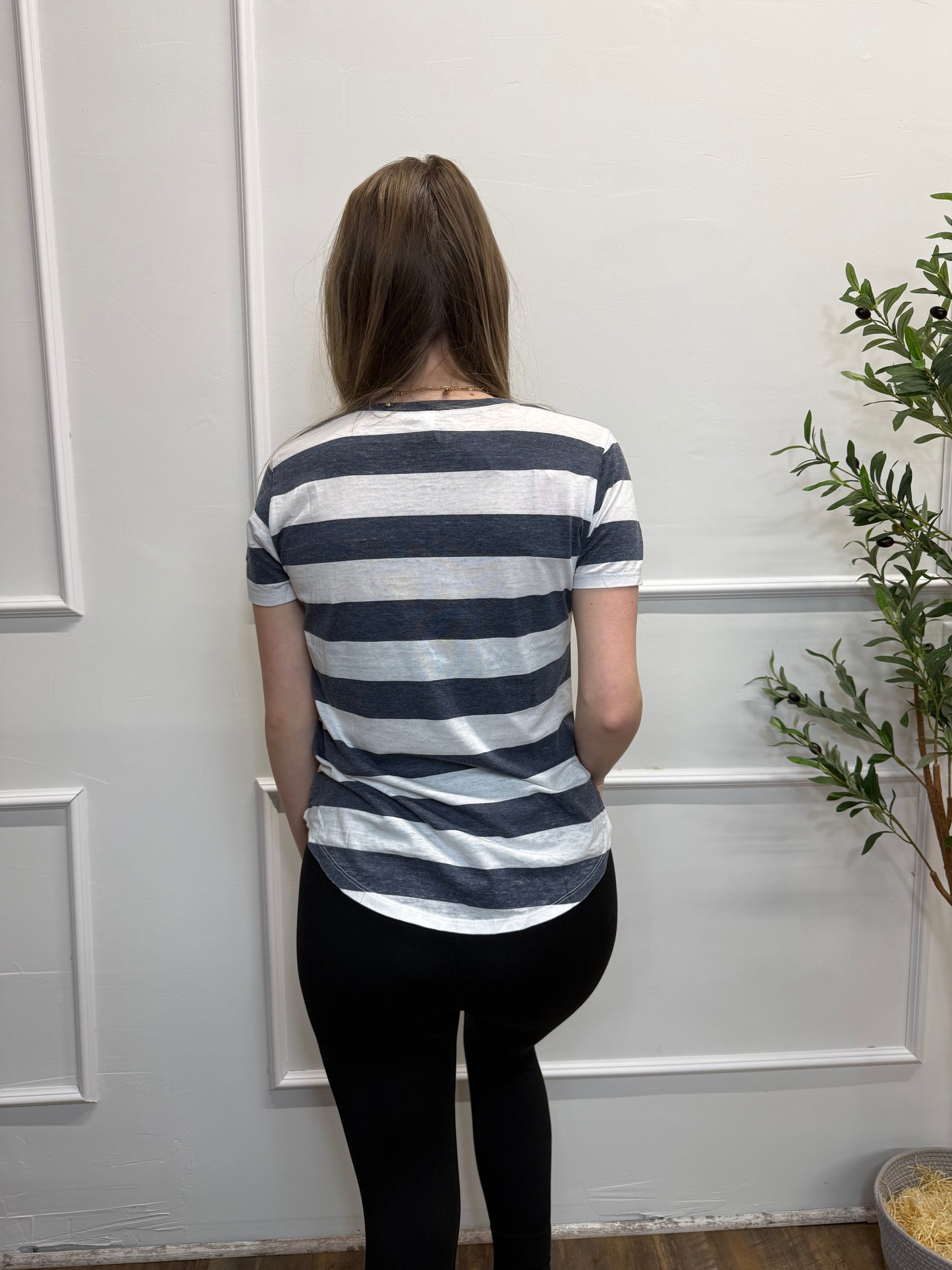Person wearing a striped shirt and black pants standing against a white door.