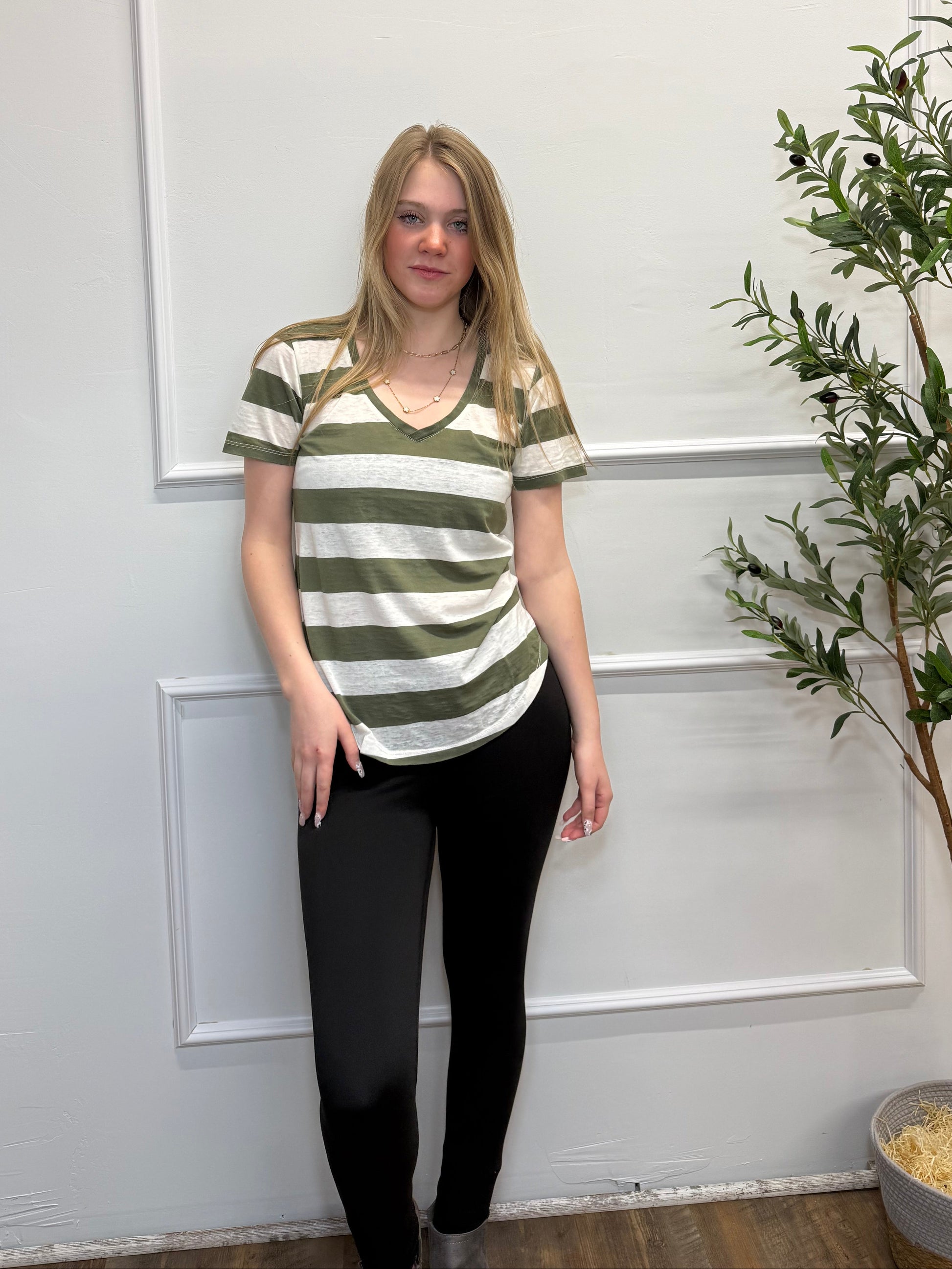 Woman wearing a striped shirt and black pants standing in front of a white door with a plant in the background.
