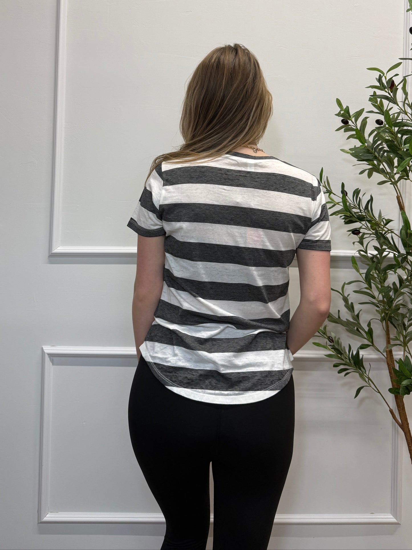Person wearing a black and white striped shirt and black pants standing in front of a white door with a plant above.
