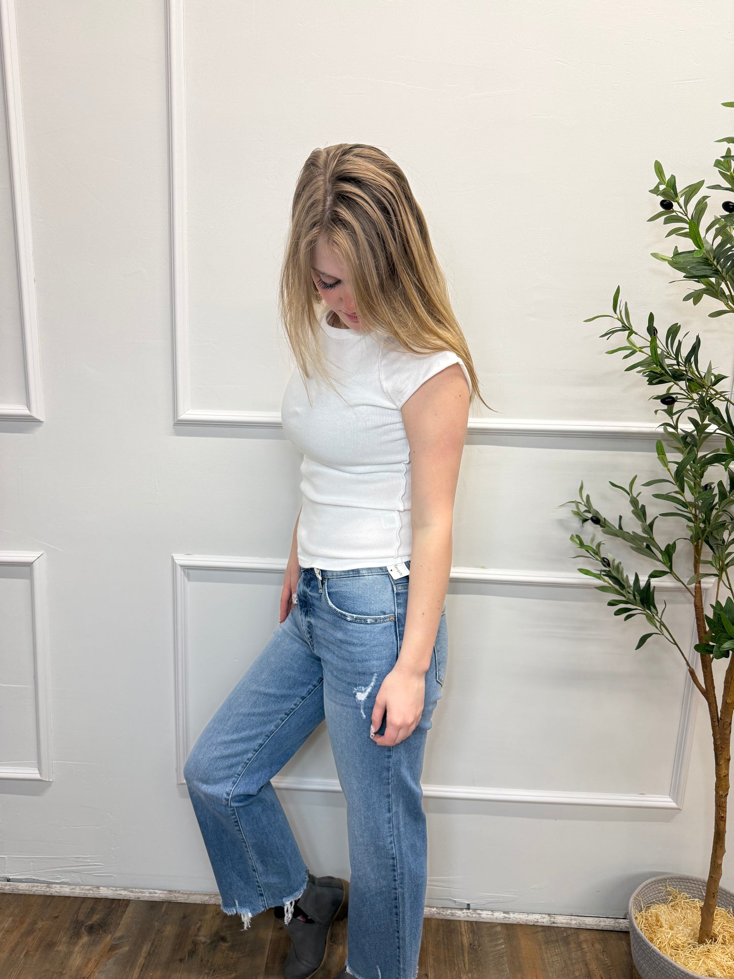 Person wearing a white top and blue jeans standing in front of a white paneled wall.