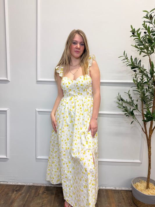 Woman wearing a yellow floral dress standing in front of a white door.