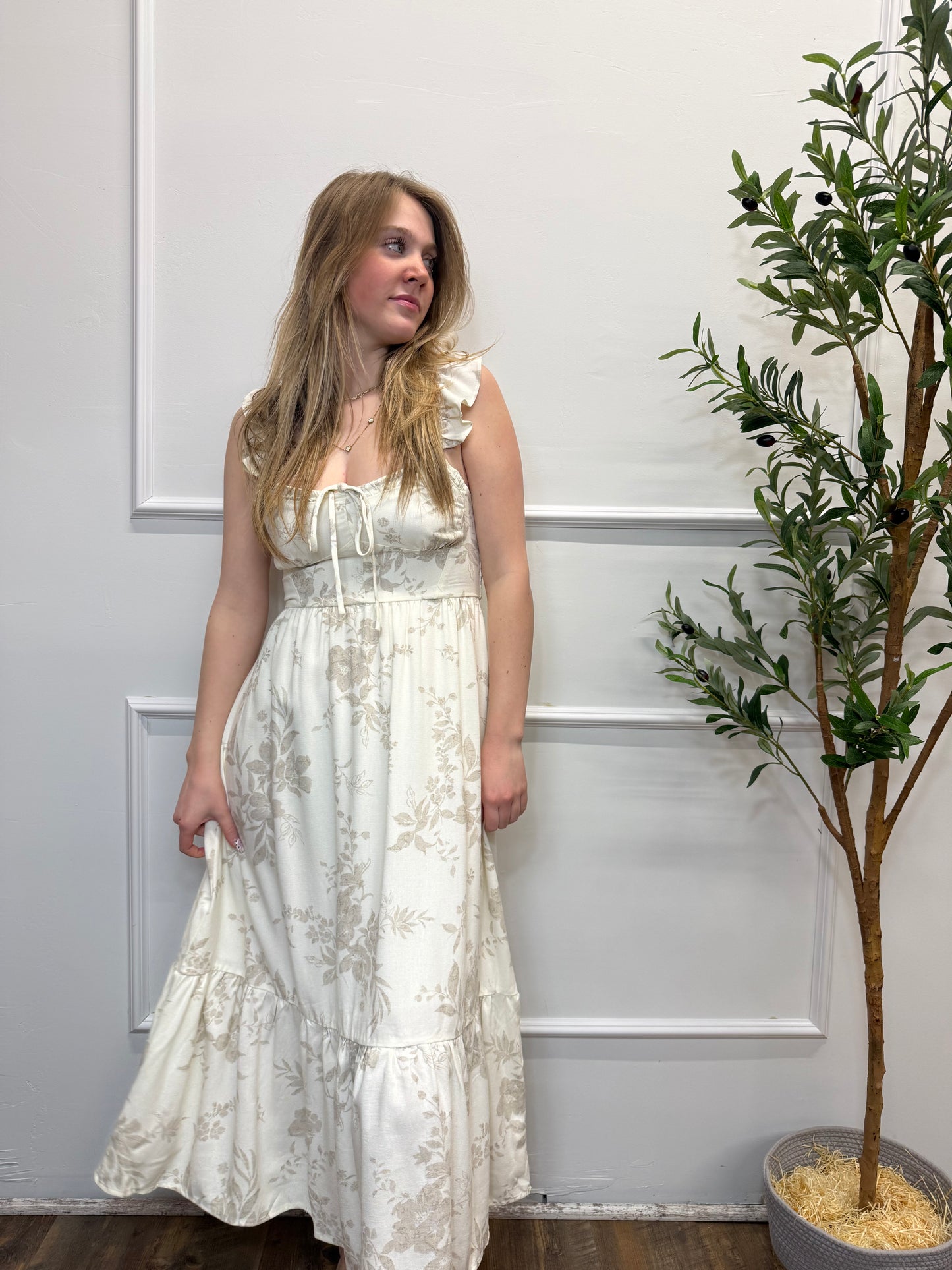 Woman in a white lace dress standing against a white wall with a plant in the background