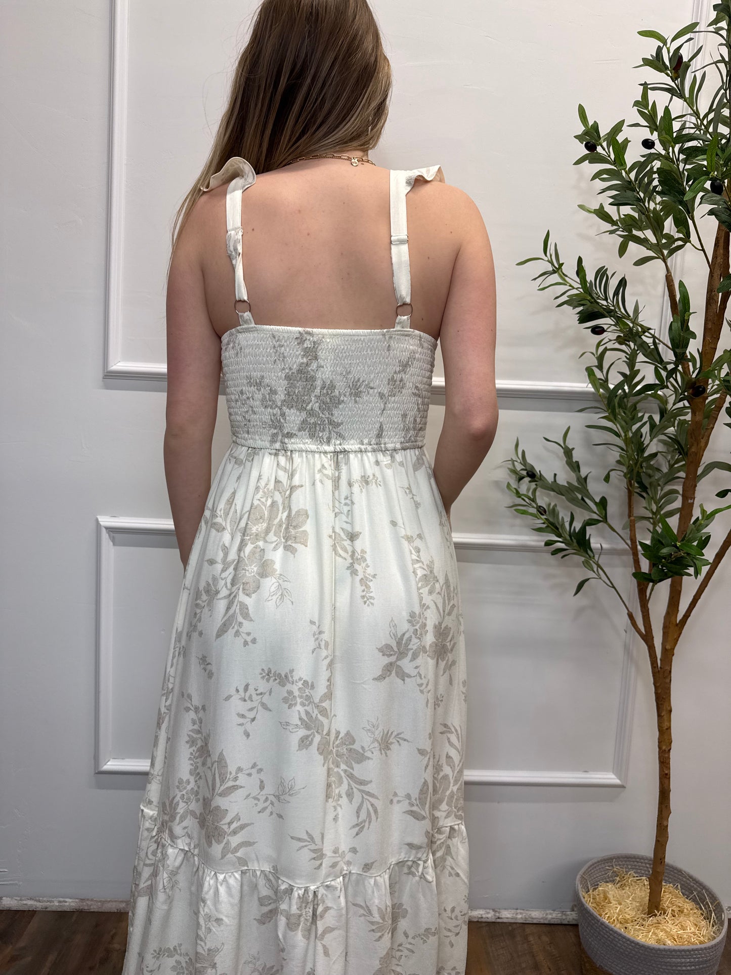 Woman wearing a floral dress standing against a white wall with decorative elements.