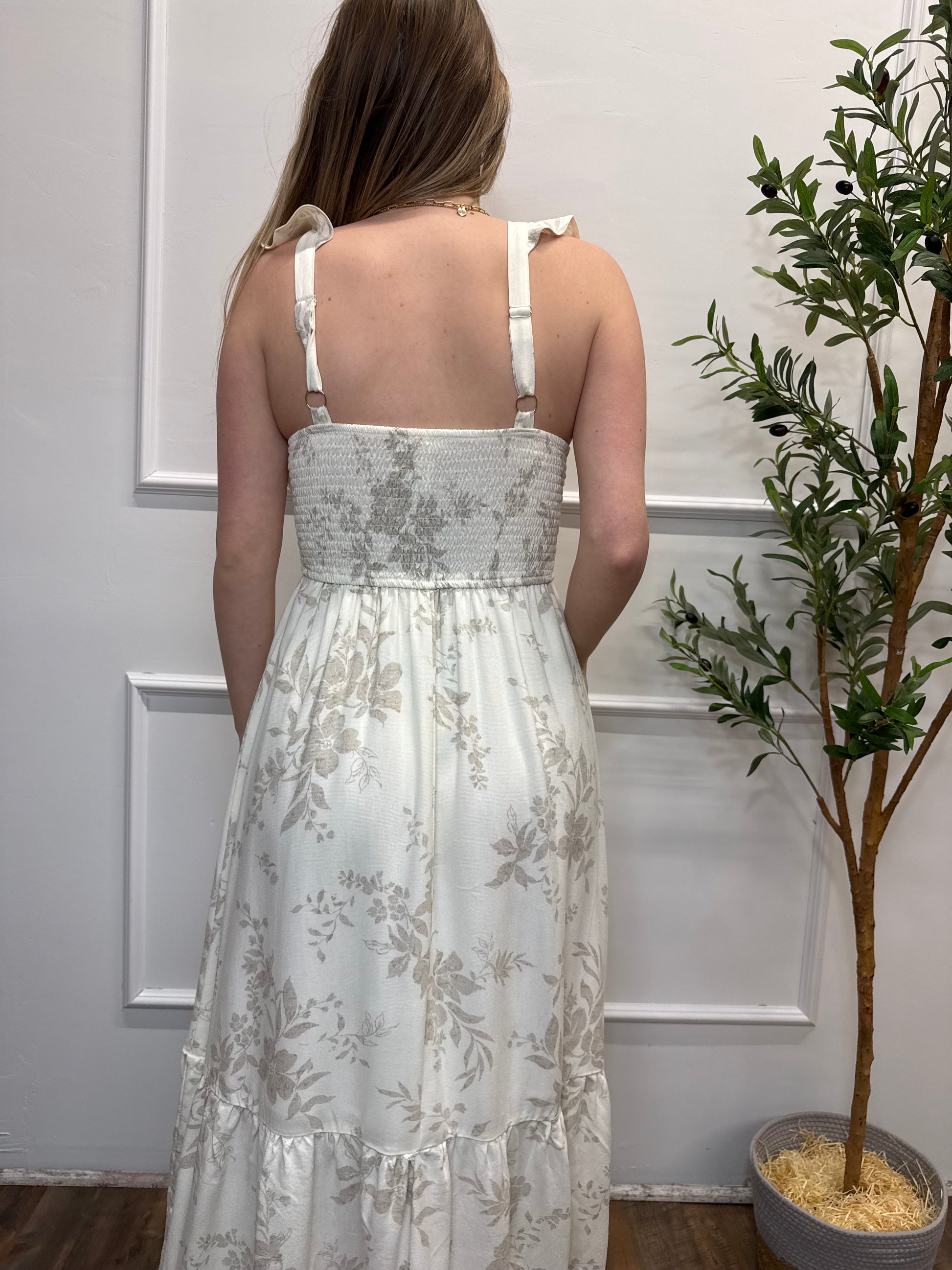 Woman wearing a floral dress standing against a white wall with decorative elements.