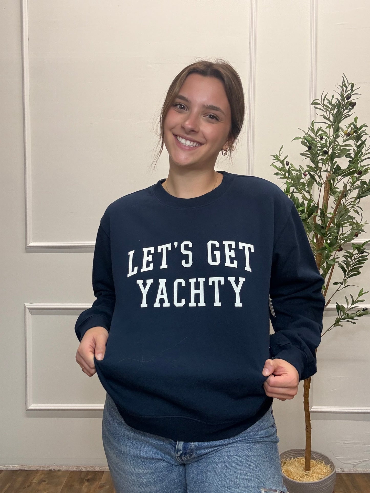 Person wearing a navy sweatshirt with 'LET'S GET YACHTY' text, standing indoors.