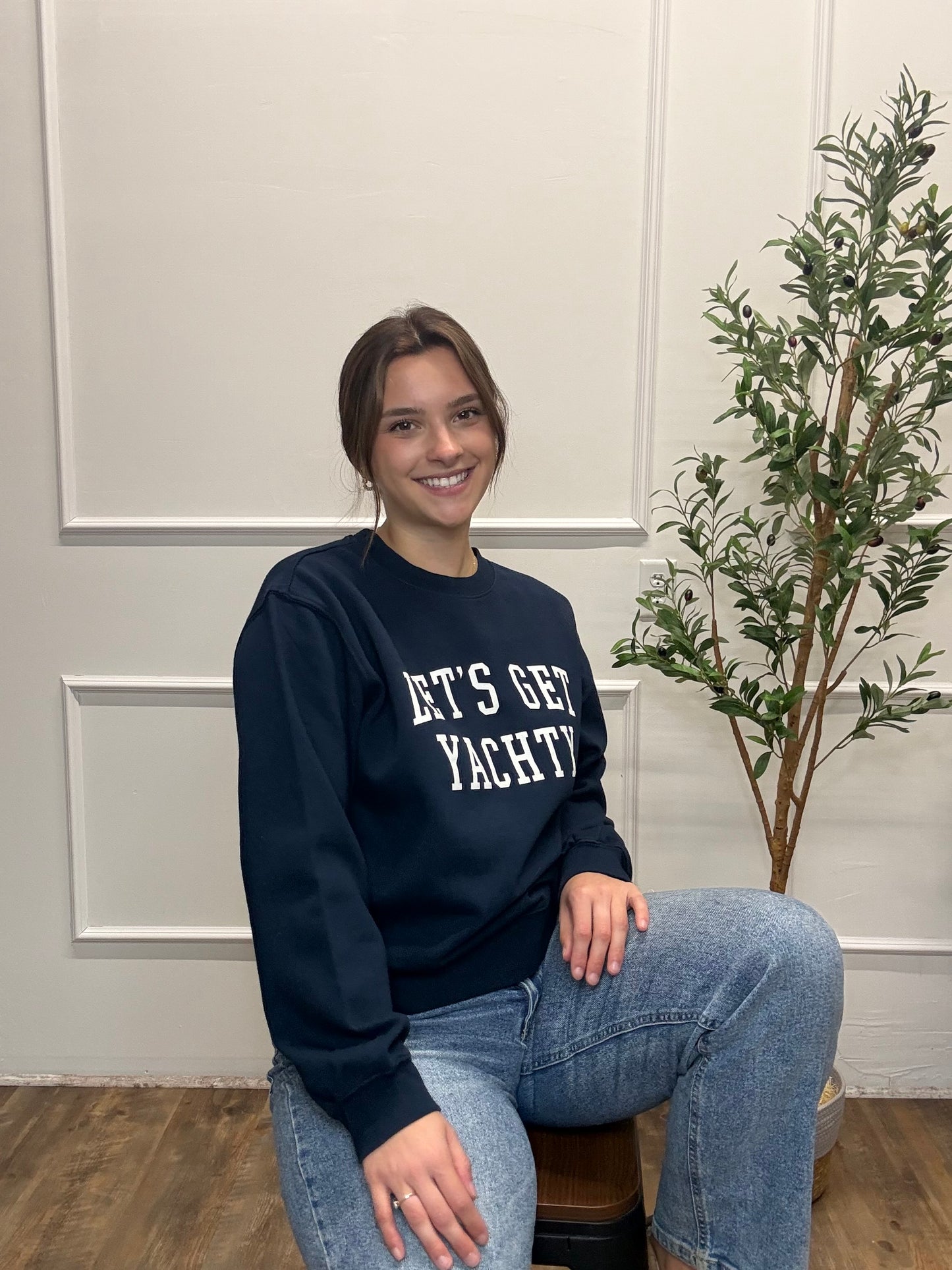 Person wearing a navy sweatshirt with text, sitting in a room with a plant and panel walls.
