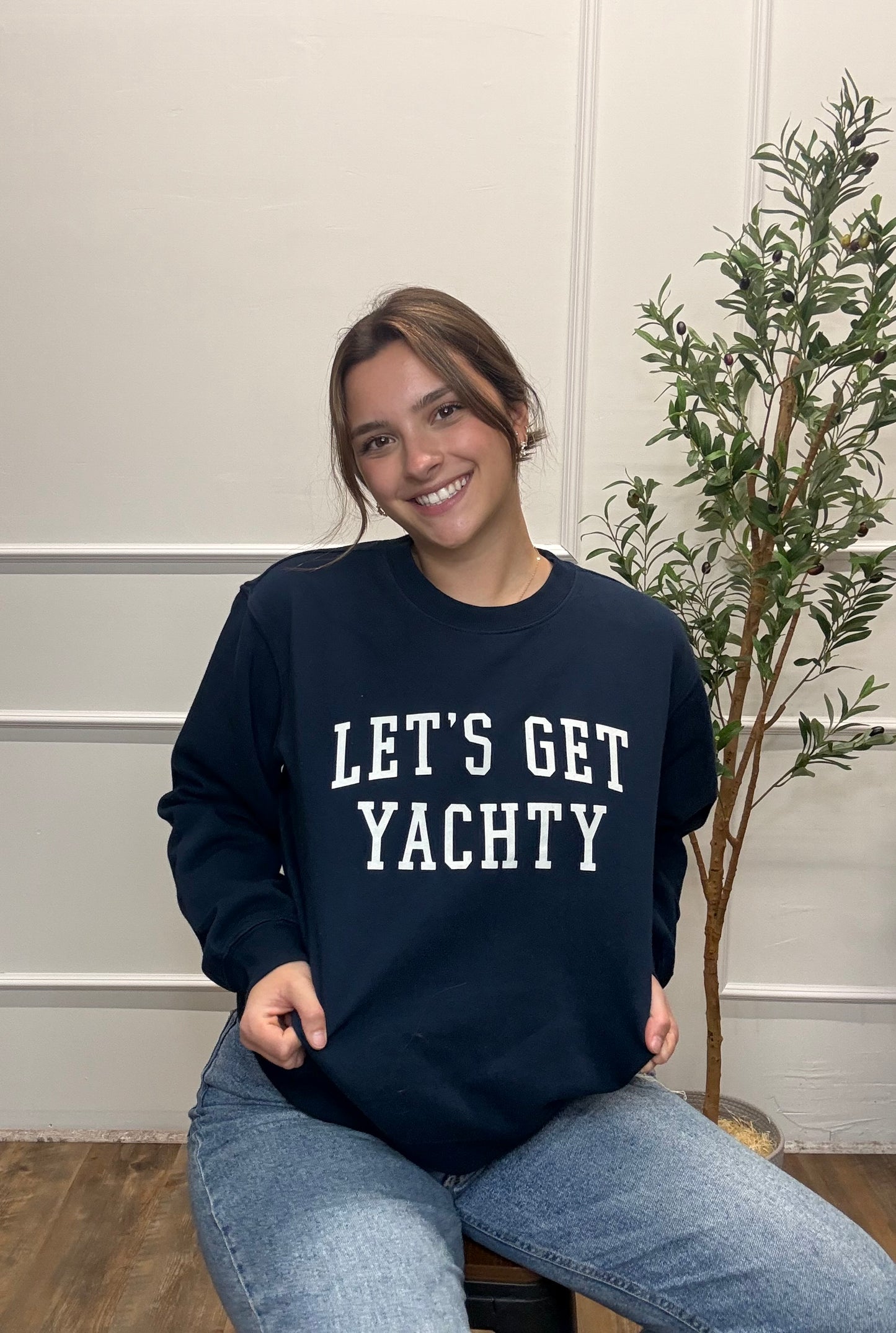 Person wearing a navy sweatshirt with 'LET'S GET YACHTY' text, sitting indoors.