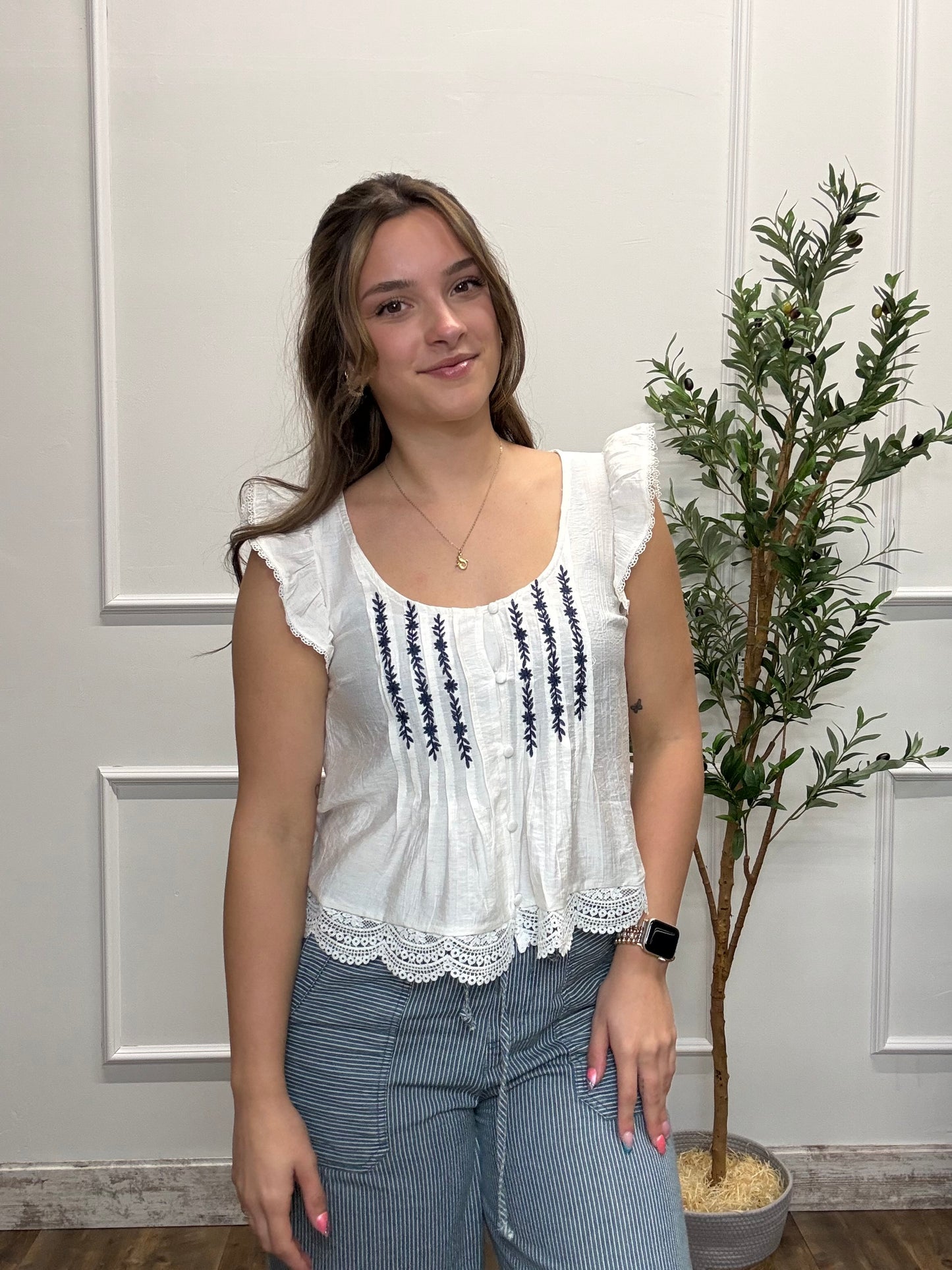 Woman wearing a white blouse with black details and blue jeans standing in front of a decorative wall.