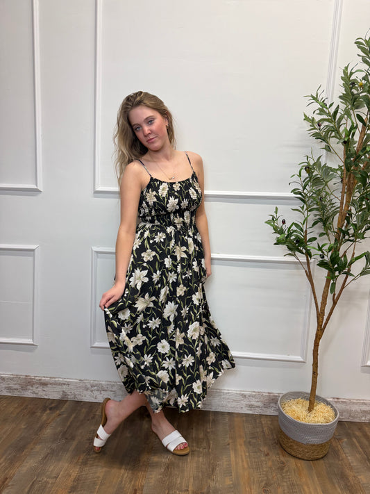 Woman in a floral dress standing in a room with a plant and wooden floor.