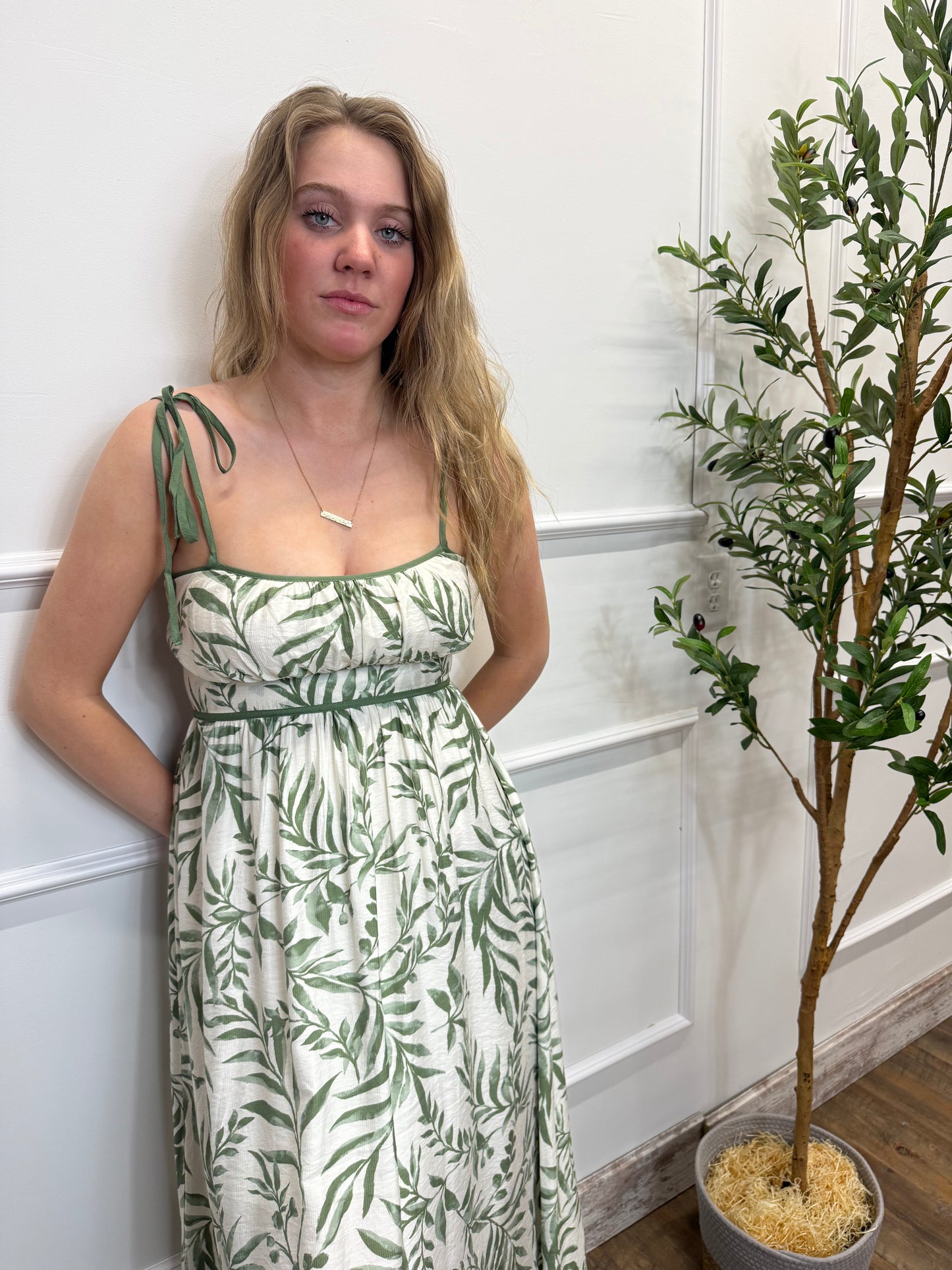 Woman in a green and white patterned dress lying on a white floor with plants in the background