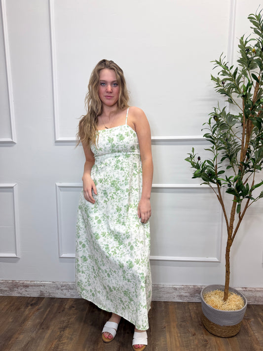 Woman wearing a floral dress standing in a room with a plant and wooden floor.