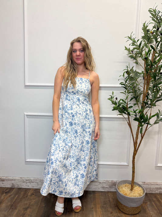 Woman in a floral dress standing in front of a white door with a plant in the background.