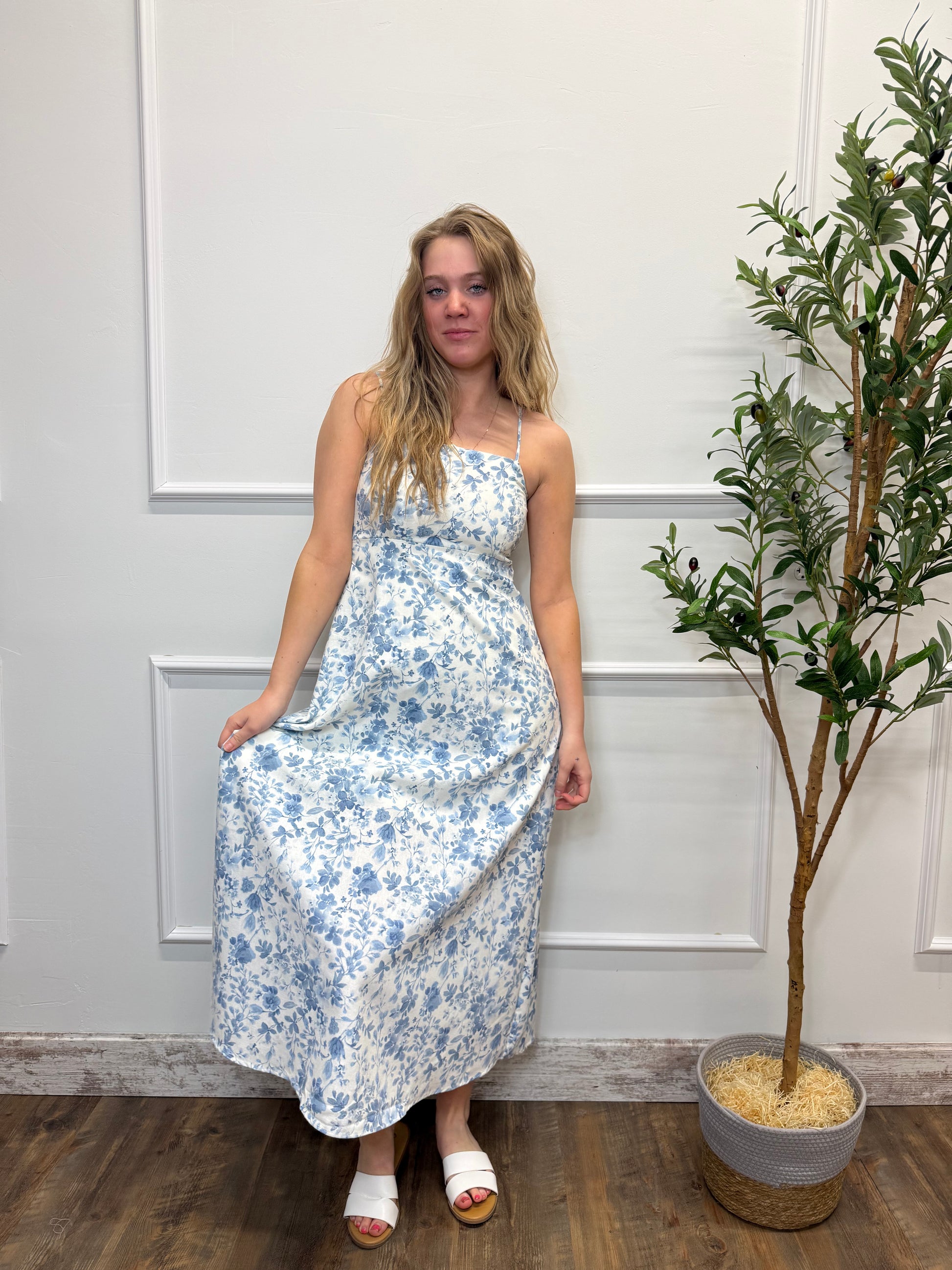 Woman in a floral dress standing in front of a white door with a plant in the background.