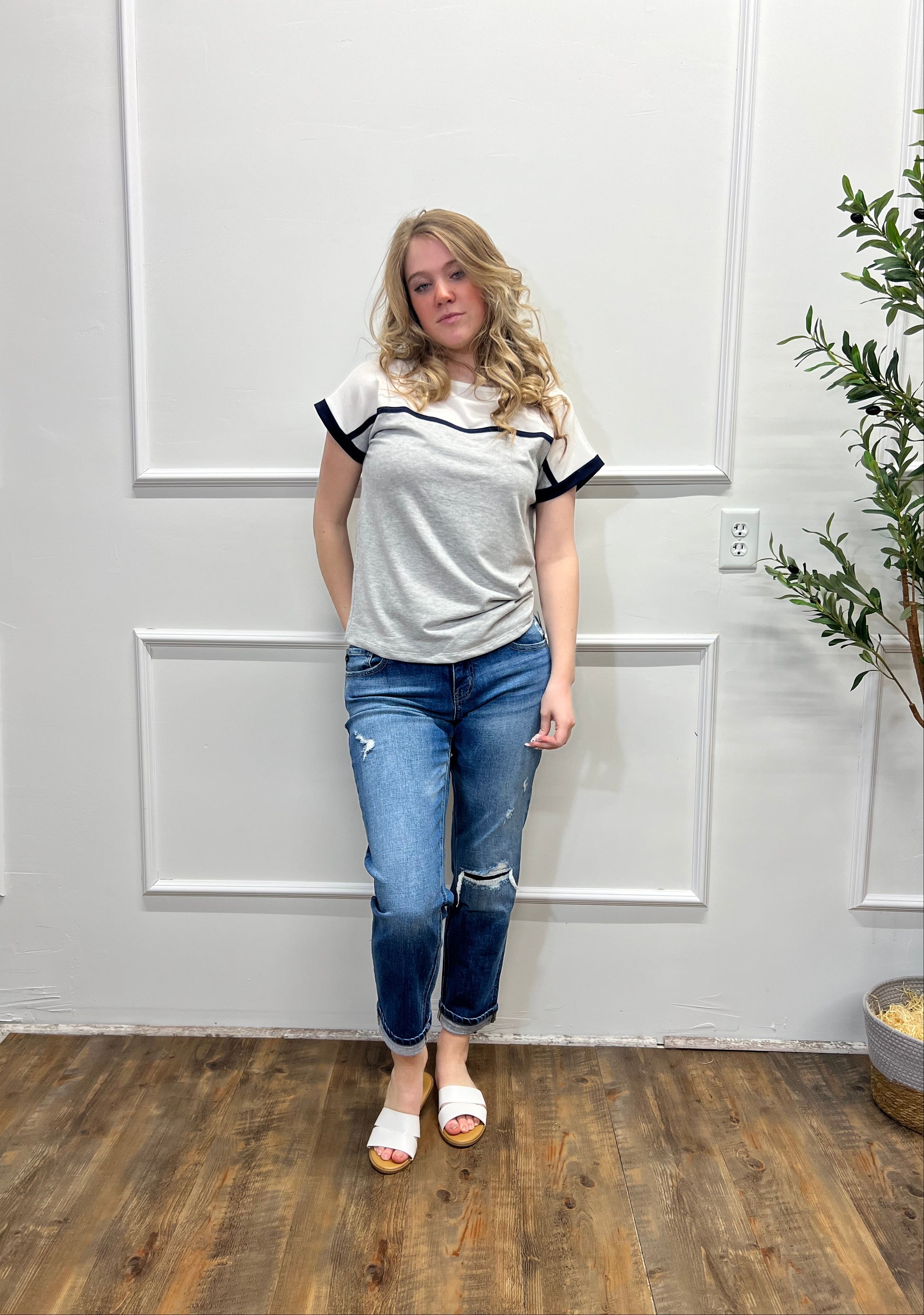 Person wearing a gray hoodie and blue jeans standing in a room with white walls and wooden flooring.