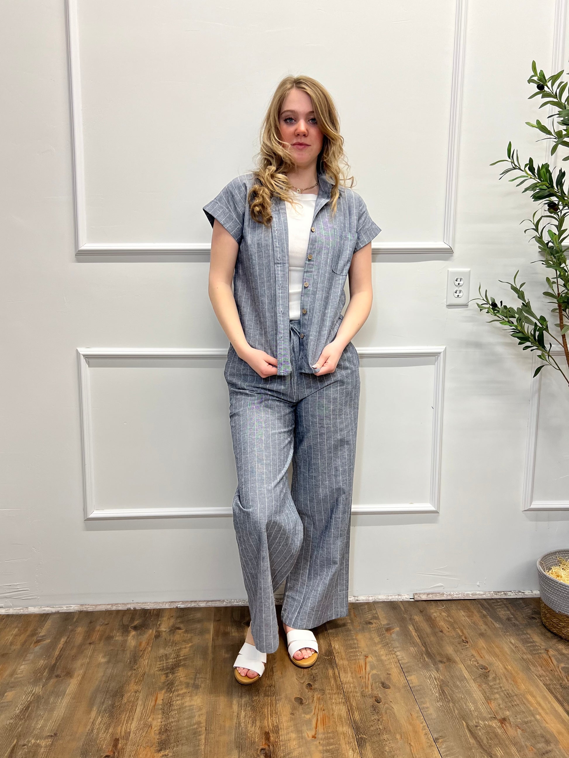 Woman wearing a blue checkered outfit standing in a room with wooden flooring and a plant.
