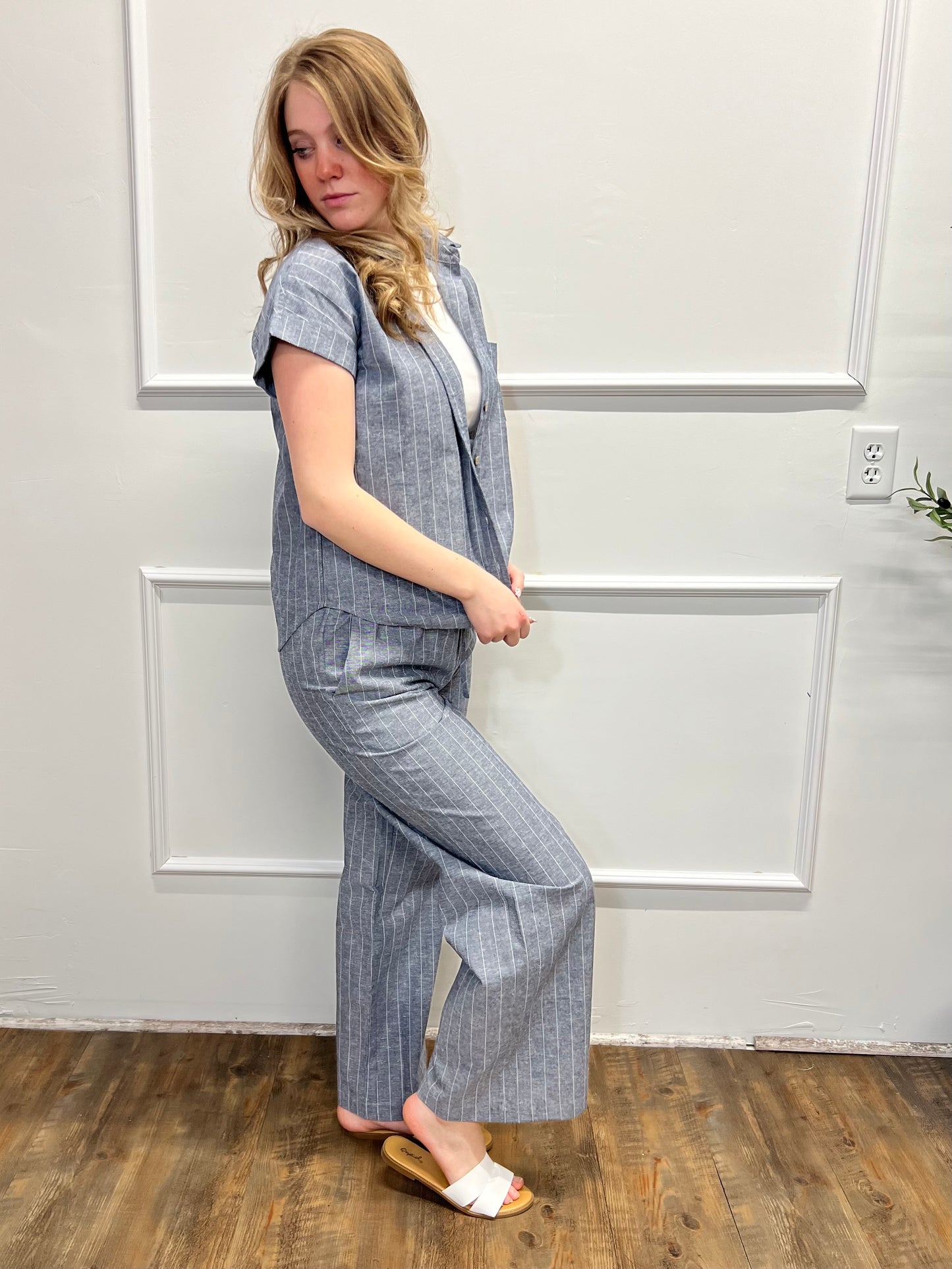 Woman wearing a gray checkered outfit standing in a room with white walls and wooden flooring.