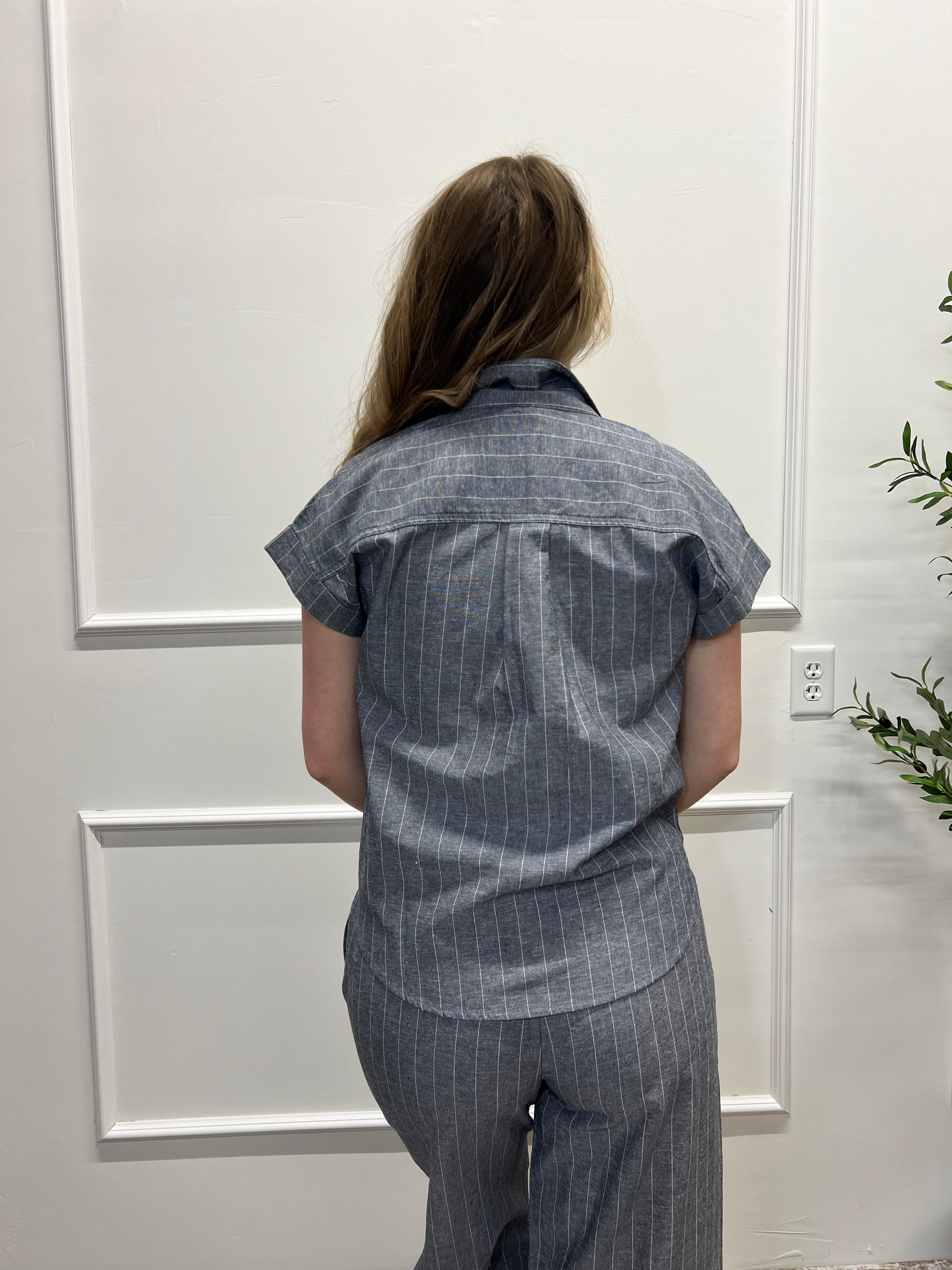 Person wearing a blue checkered shirt and pants standing in front of white doors.