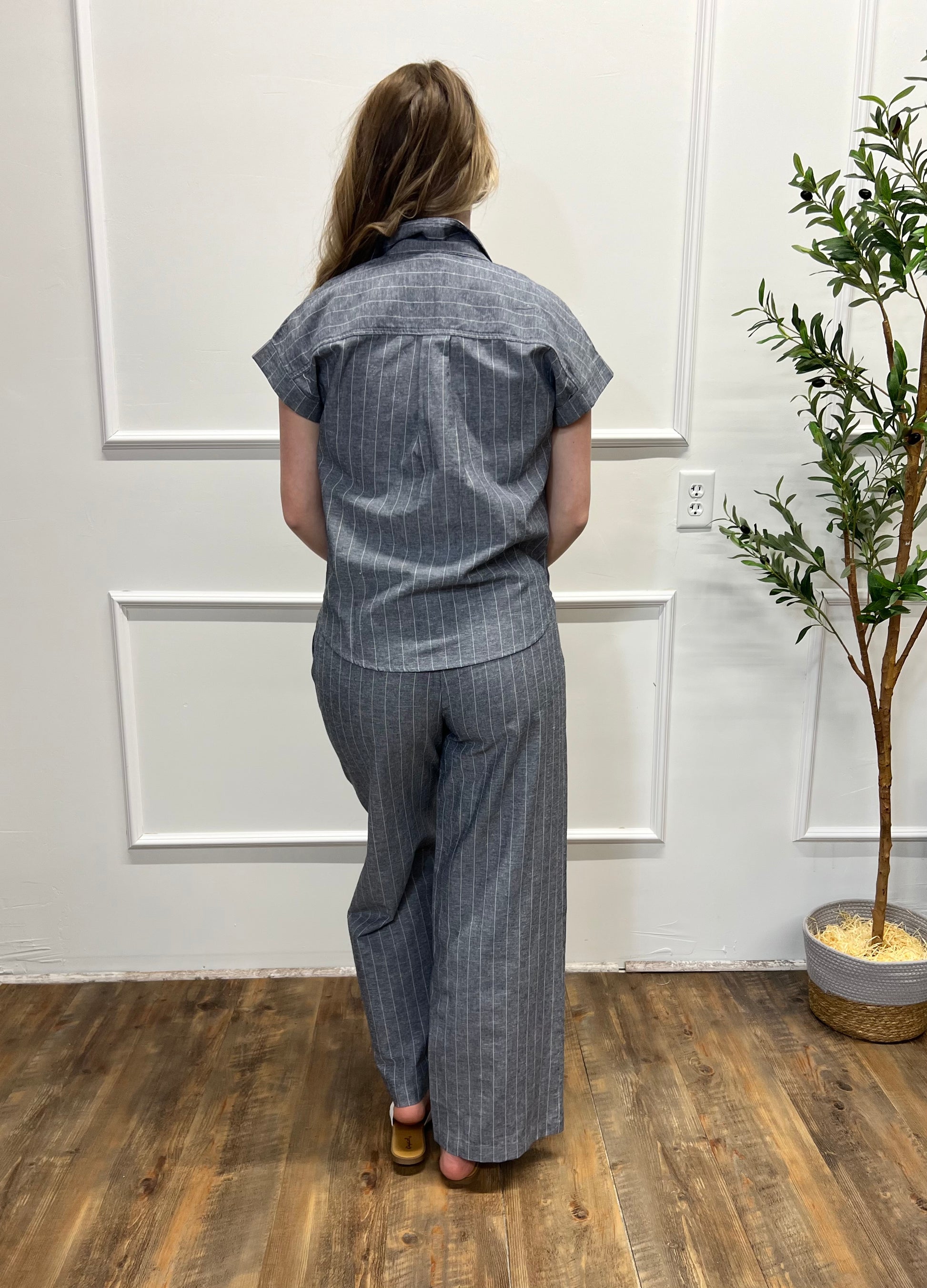 Person wearing a gray striped outfit standing in a room with a plant and white walls.