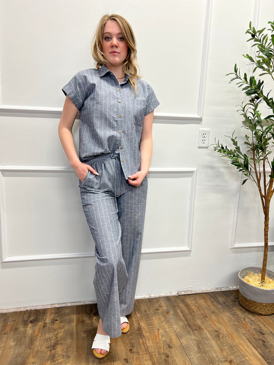 Person wearing a gray outfit standing in a room with white walls and wooden flooring.