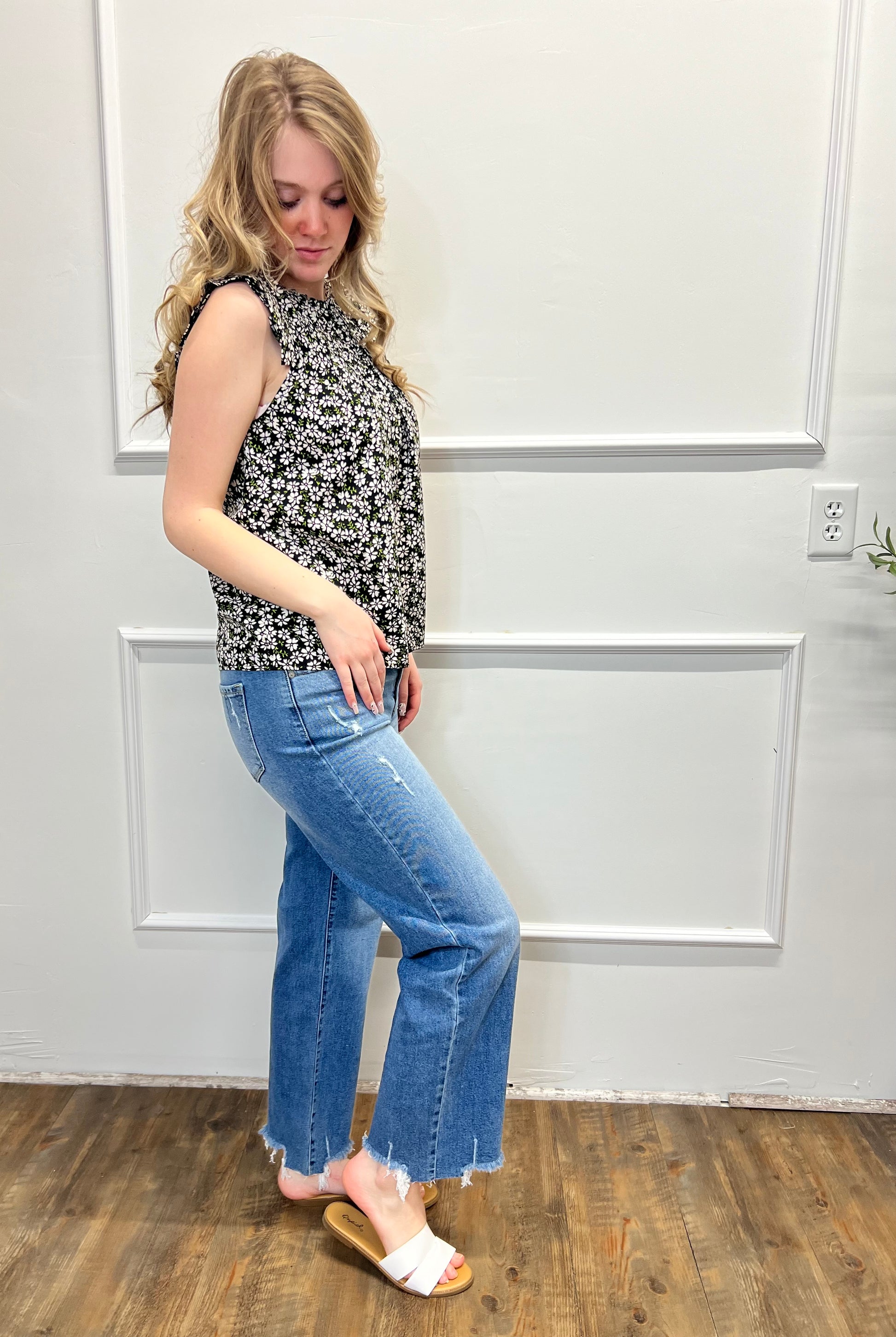 Woman wearing a floral top and blue jeans standing in a room with white paneled walls.