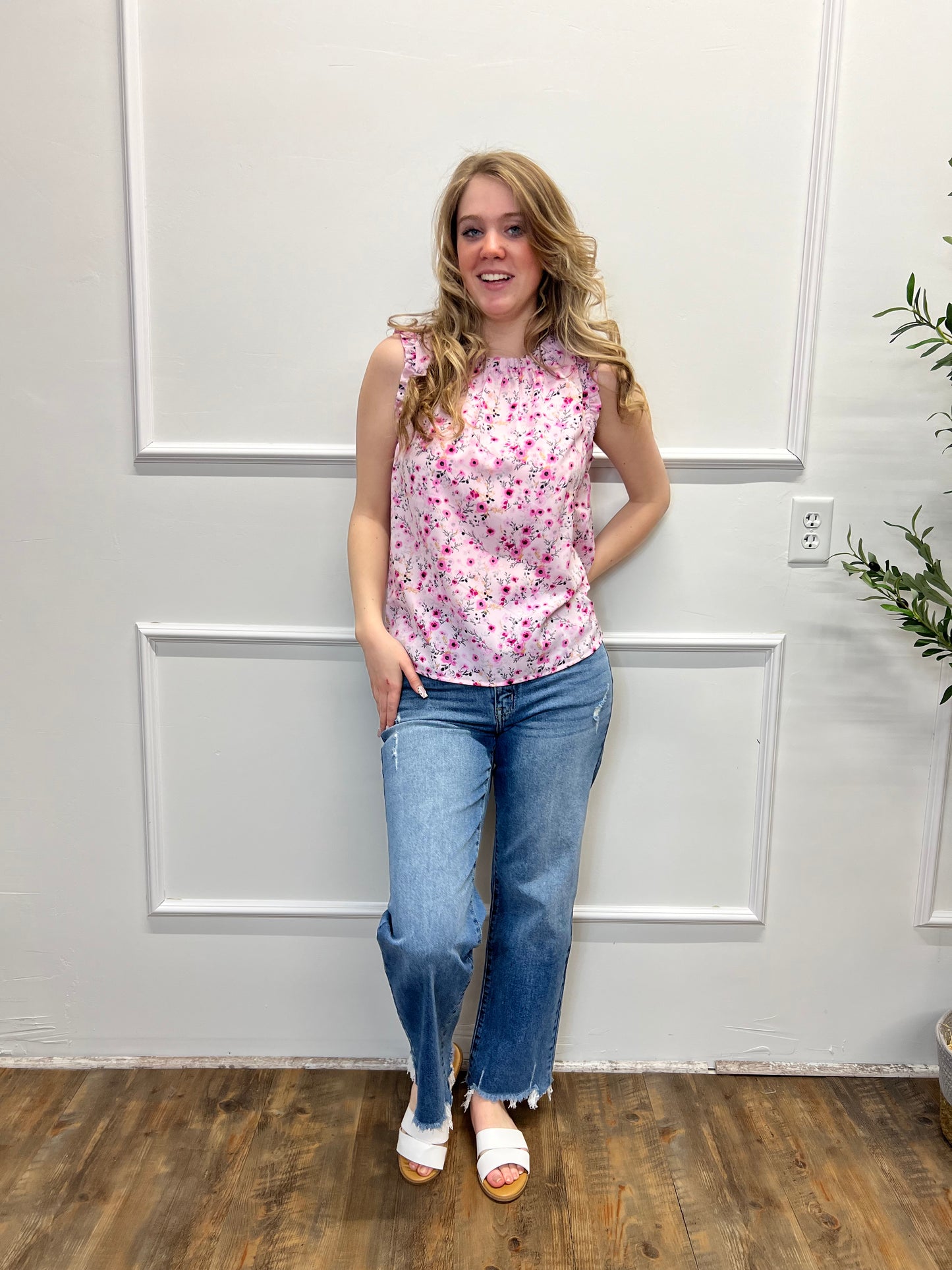 Woman in a floral top and jeans standing in a room with white paneled walls and wooden flooring.