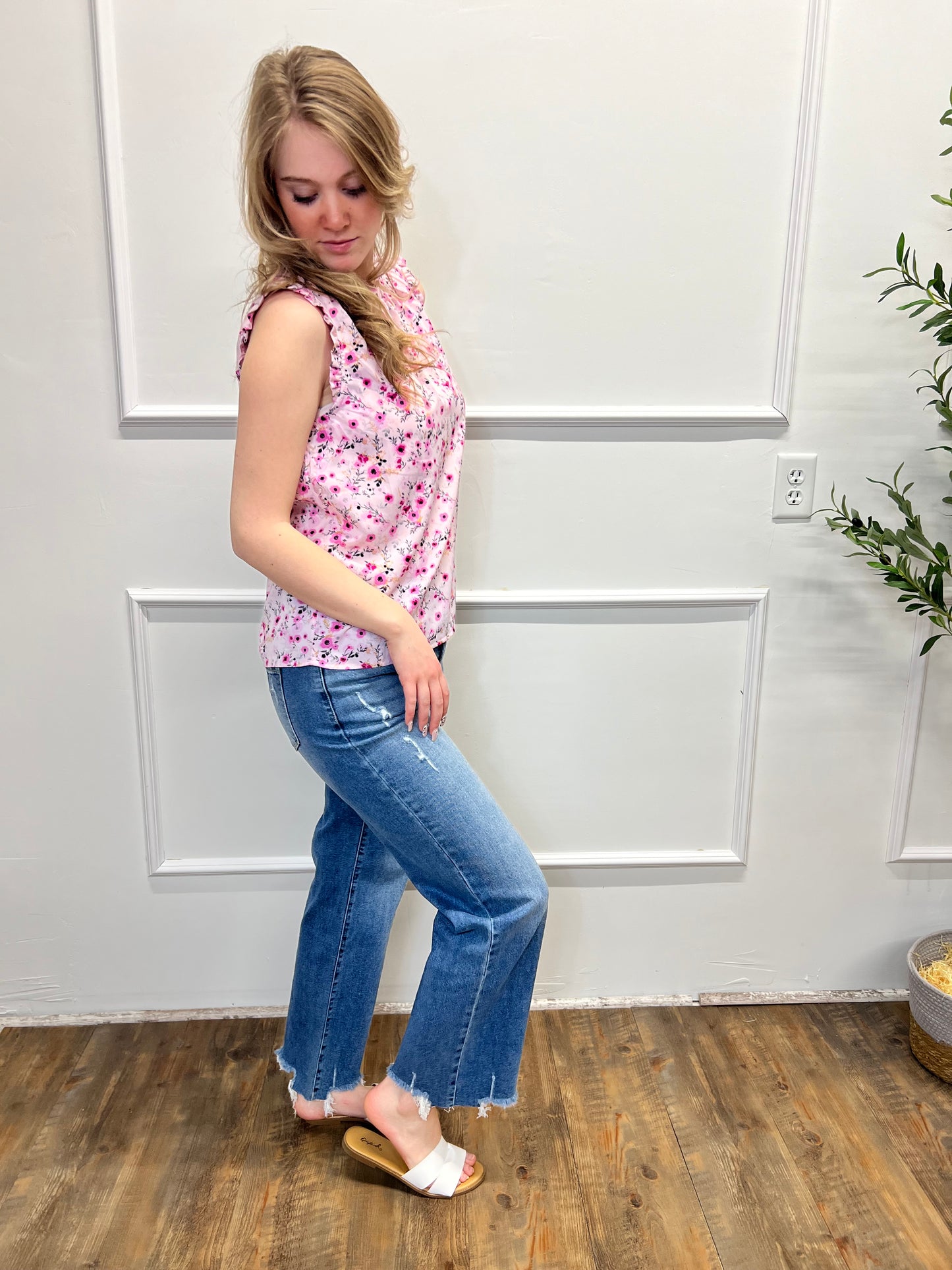 Person wearing a pink floral top and blue jeans standing on a wooden floor.