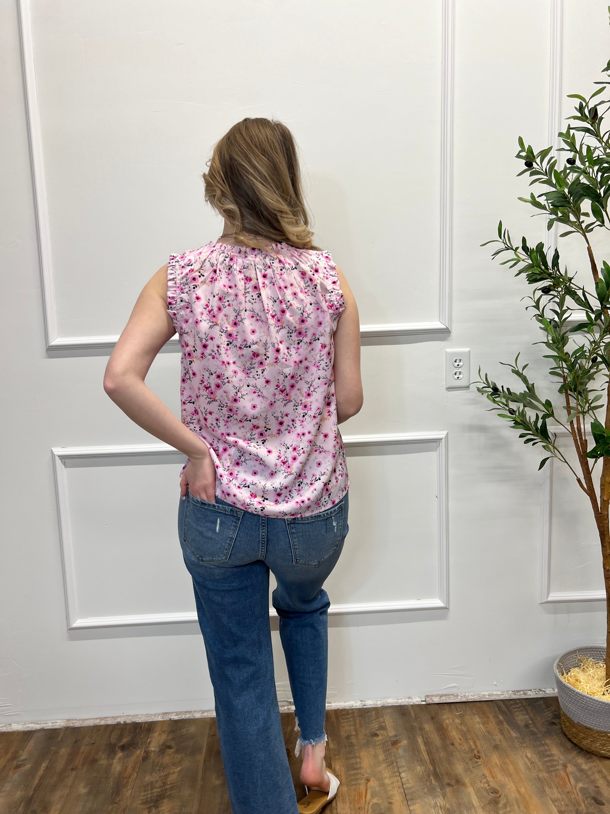 Person wearing a pink floral top and blue jeans standing in a room with white paneled walls and a wooden floor.
