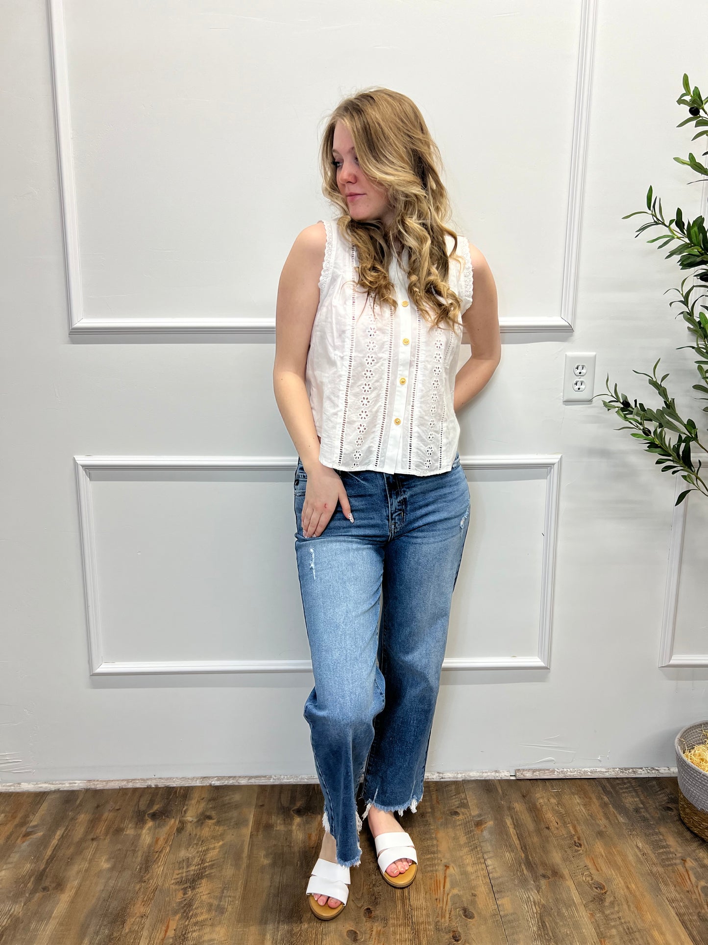 Person wearing a white lace top and blue jeans standing in a room with a wooden floor and white walls.