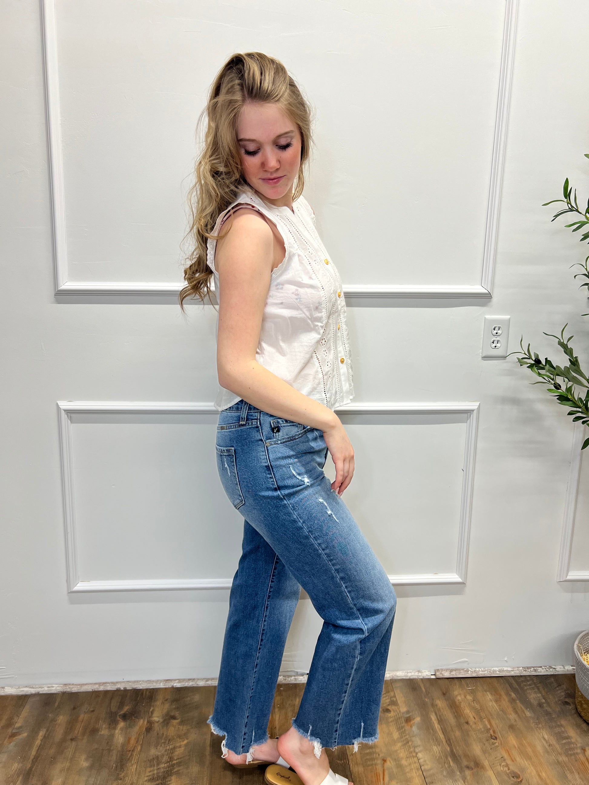 Woman in a white top and blue jeans standing against a white paneled wall.