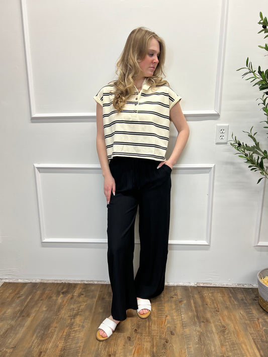 Person wearing a striped shirt and black pants standing in a room with white walls and wooden flooring.