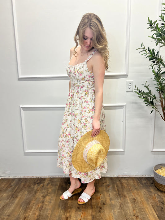 Woman in a floral dress and straw hat standing in a room with wooden floor and white walls.