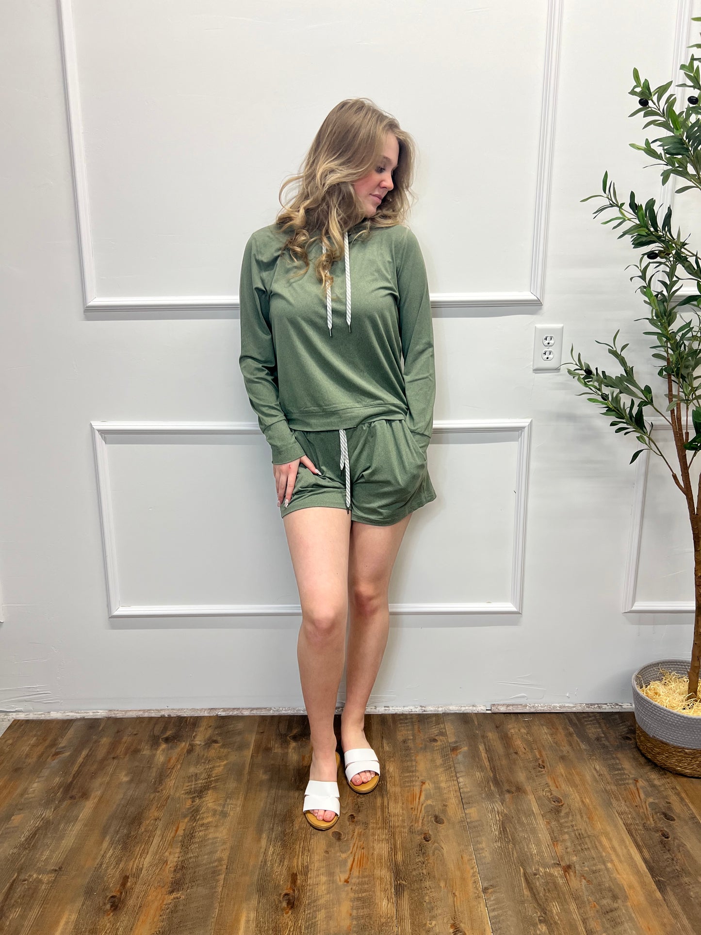 Woman in a green dress standing in a room with white walls and wooden flooring.