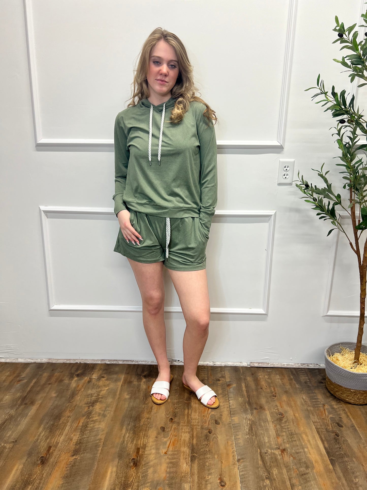 Person wearing a green outfit standing in a room with wooden flooring and white walls.