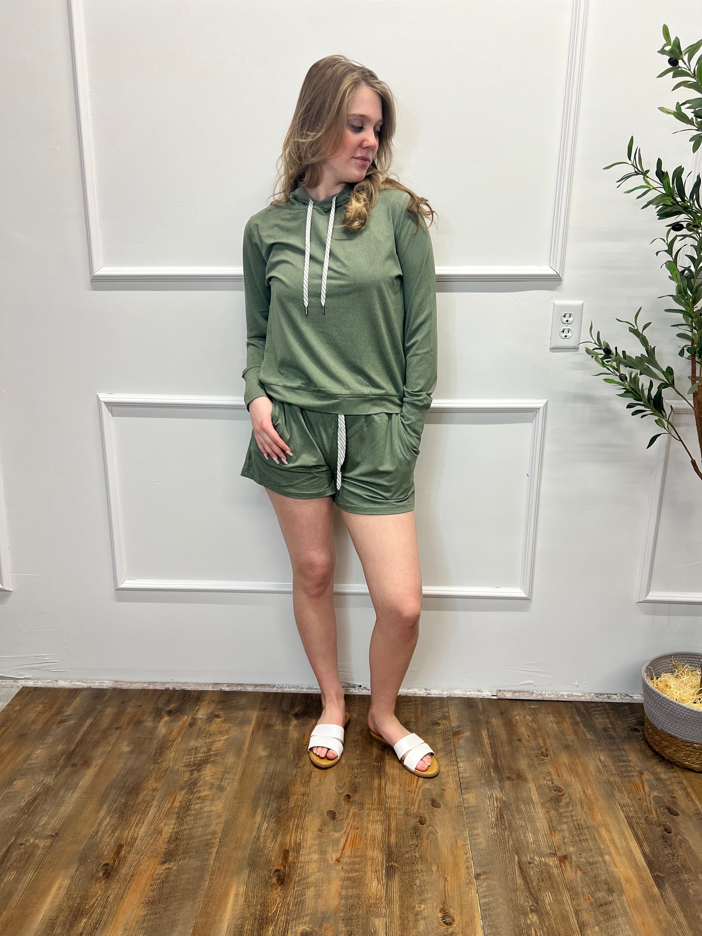 Woman wearing a green dress standing in a room with white paneled walls and wooden flooring.