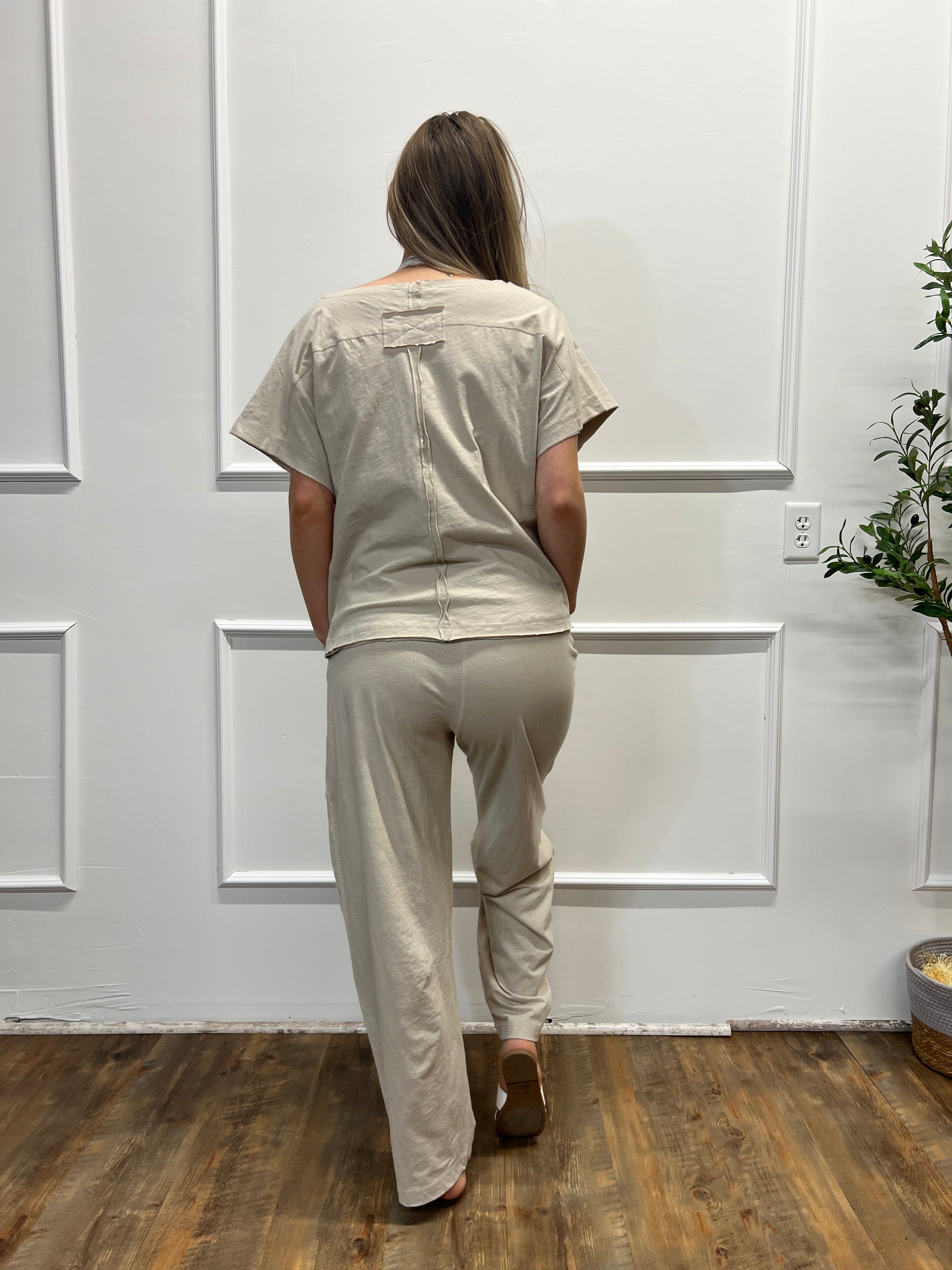 Person in a beige outfit standing in front of a white door with a wooden floor.