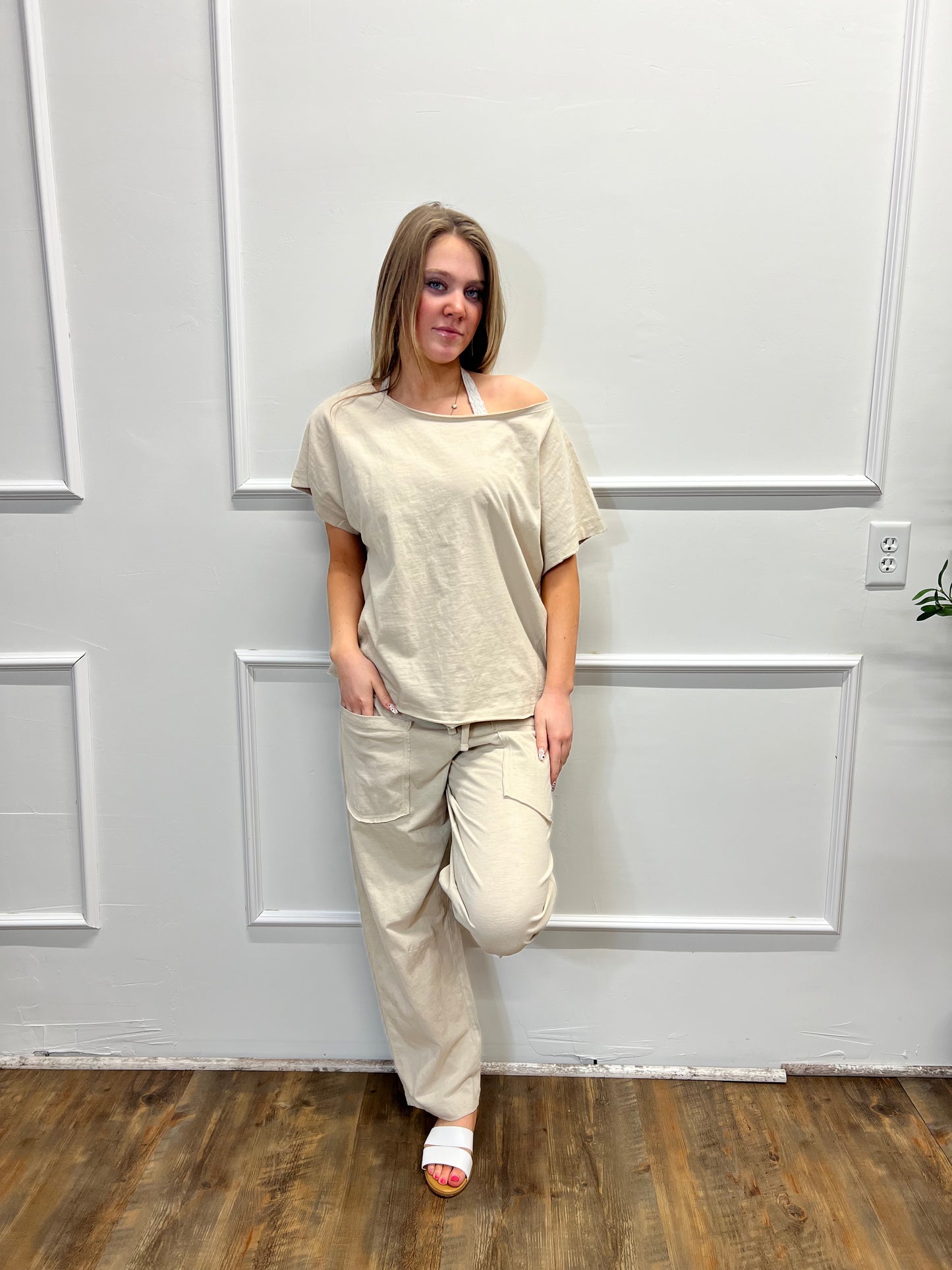 Person wearing a beige outfit standing in front of a white paneled door.