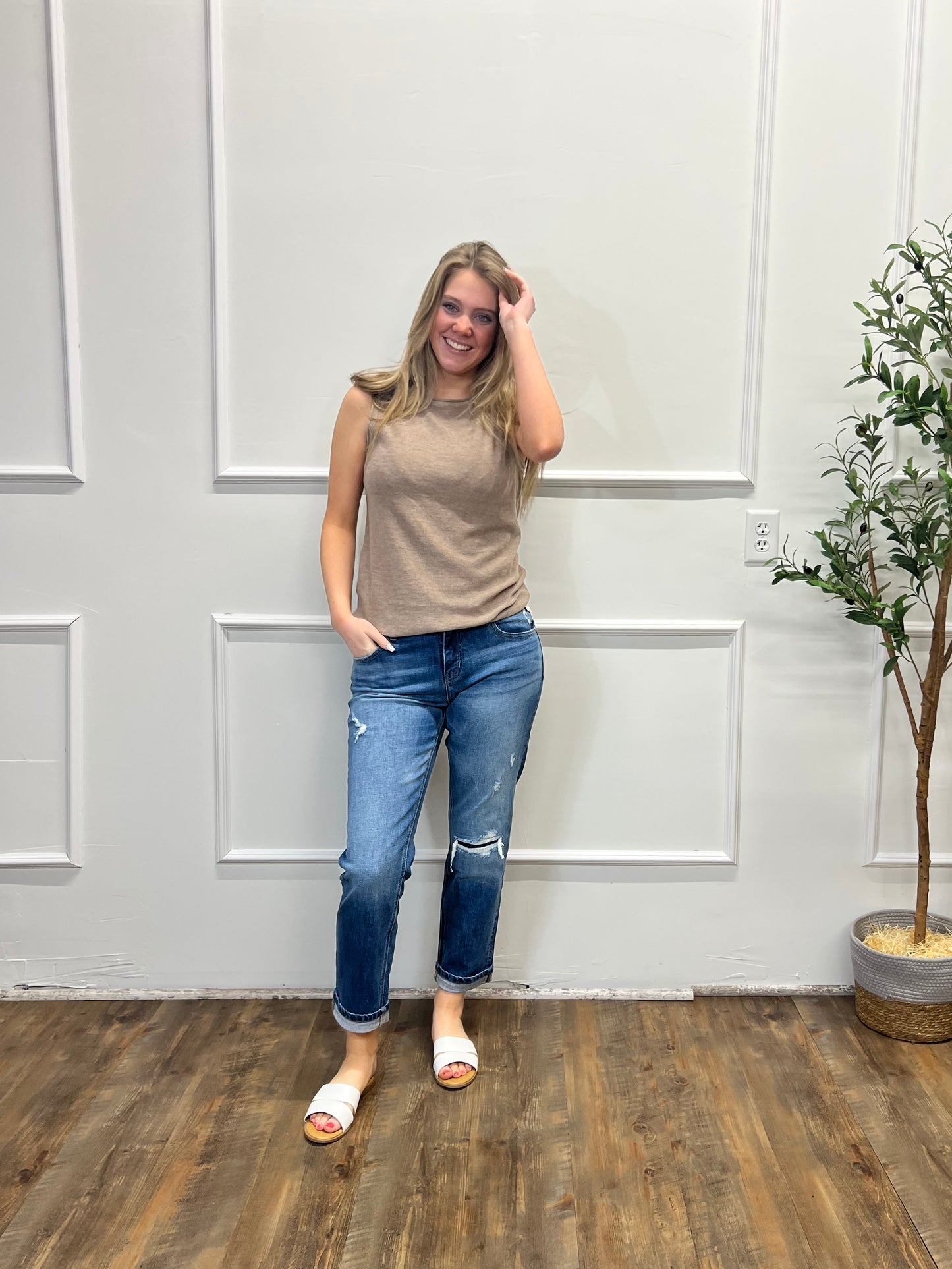 Person standing in a room with a white wall and wooden floor, next to a potted plant.