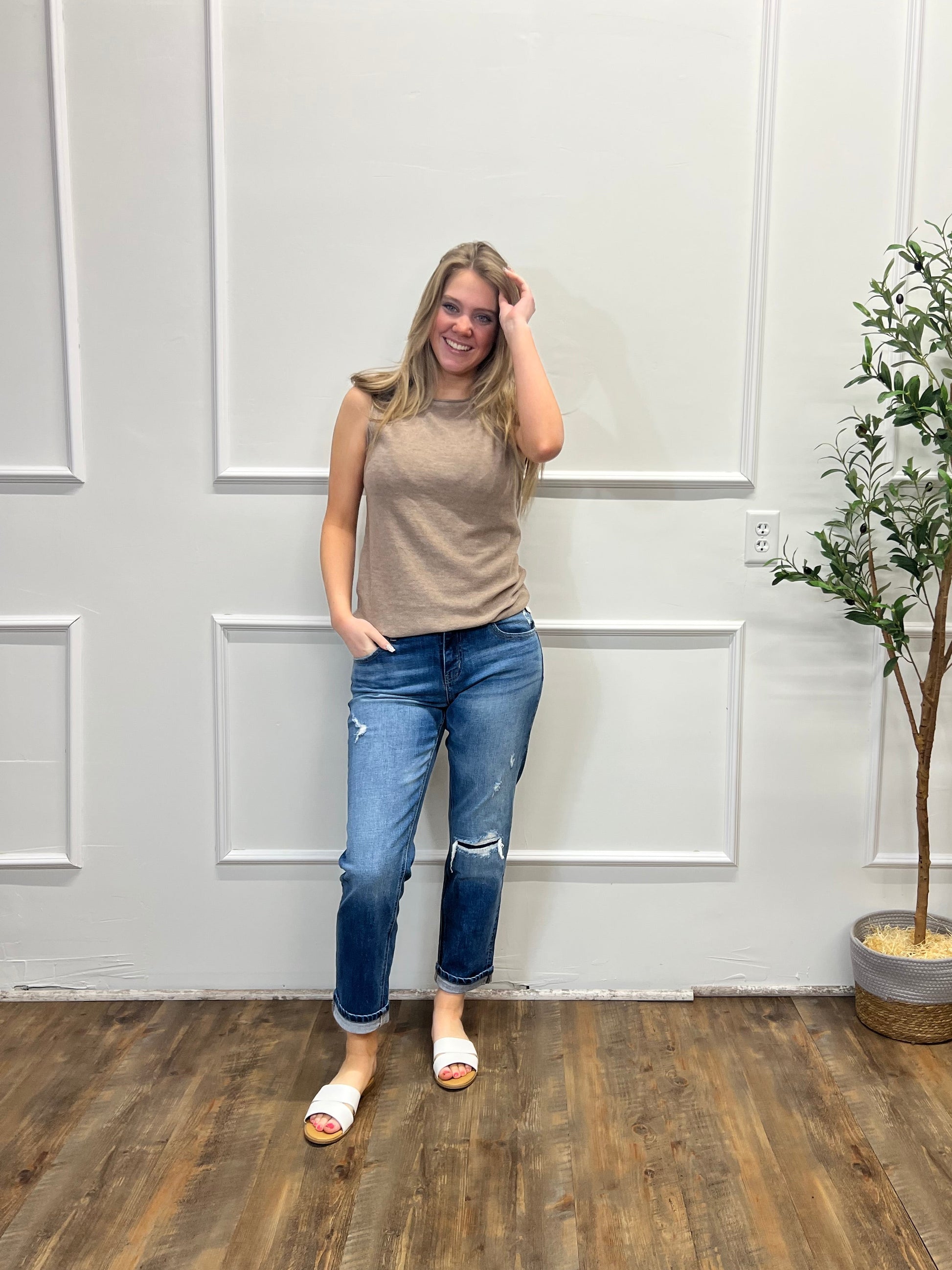 Person standing in a room with a white wall and wooden floor, next to a potted plant.