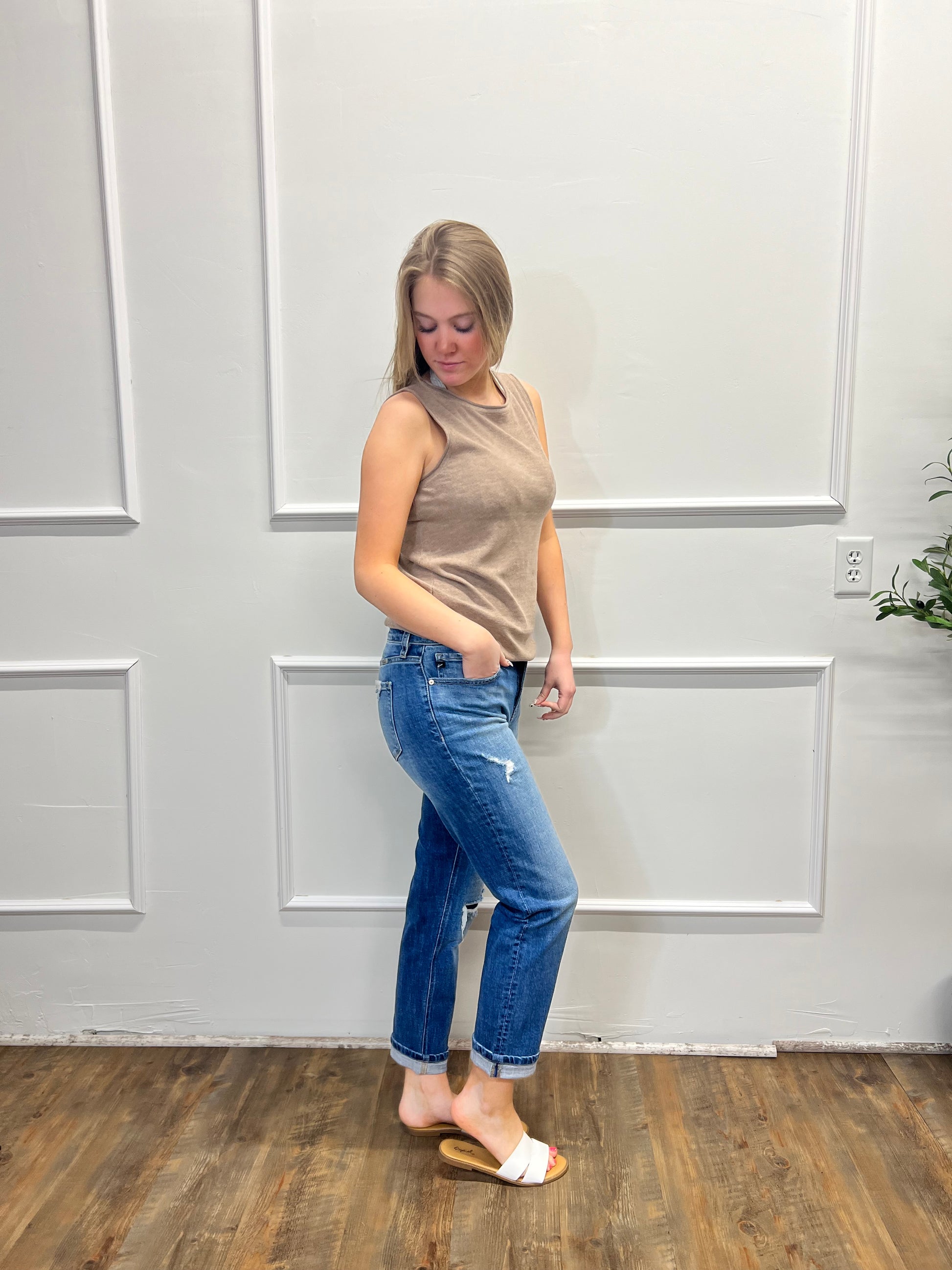 Person wearing a beige top and blue jeans standing against a white paneled wall.