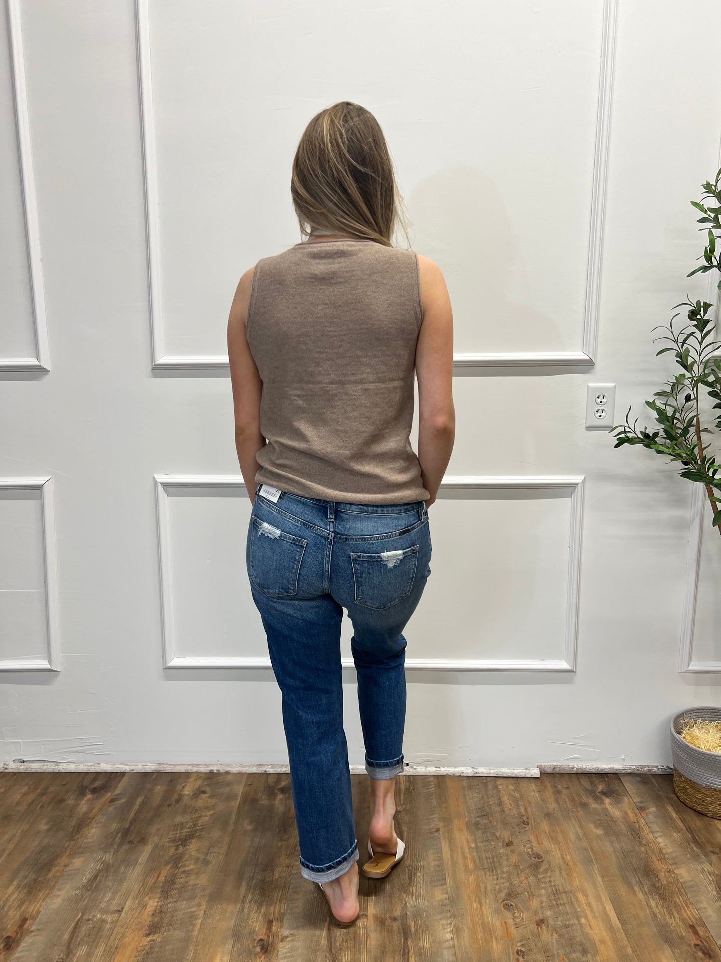 Person wearing a brown top and blue jeans standing in front of a white door.
