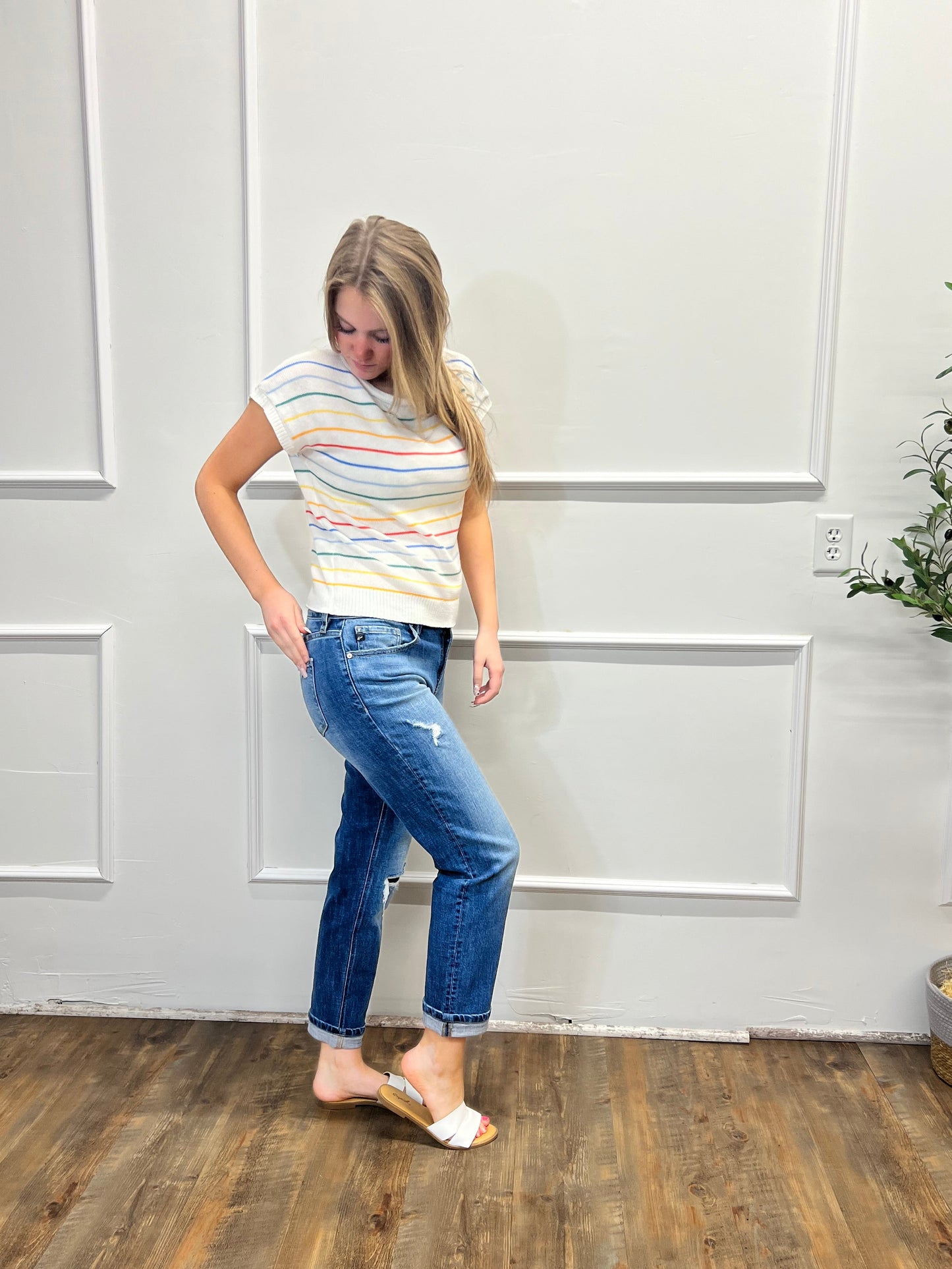 Person wearing a striped shirt and jeans standing in a room with white paneled walls and wooden flooring.
