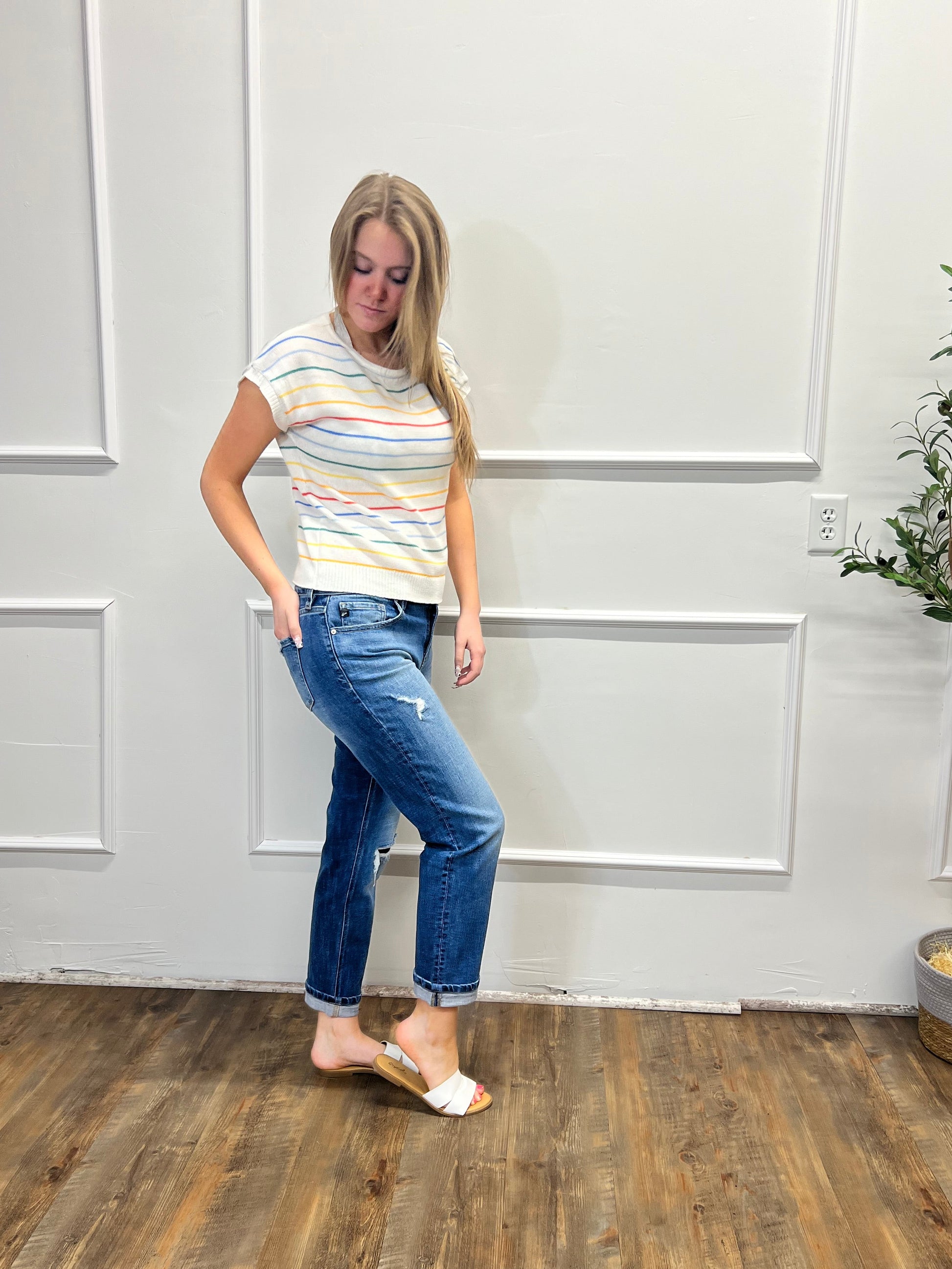 Person wearing a striped shirt and jeans standing in a room with white paneled walls and wooden flooring.