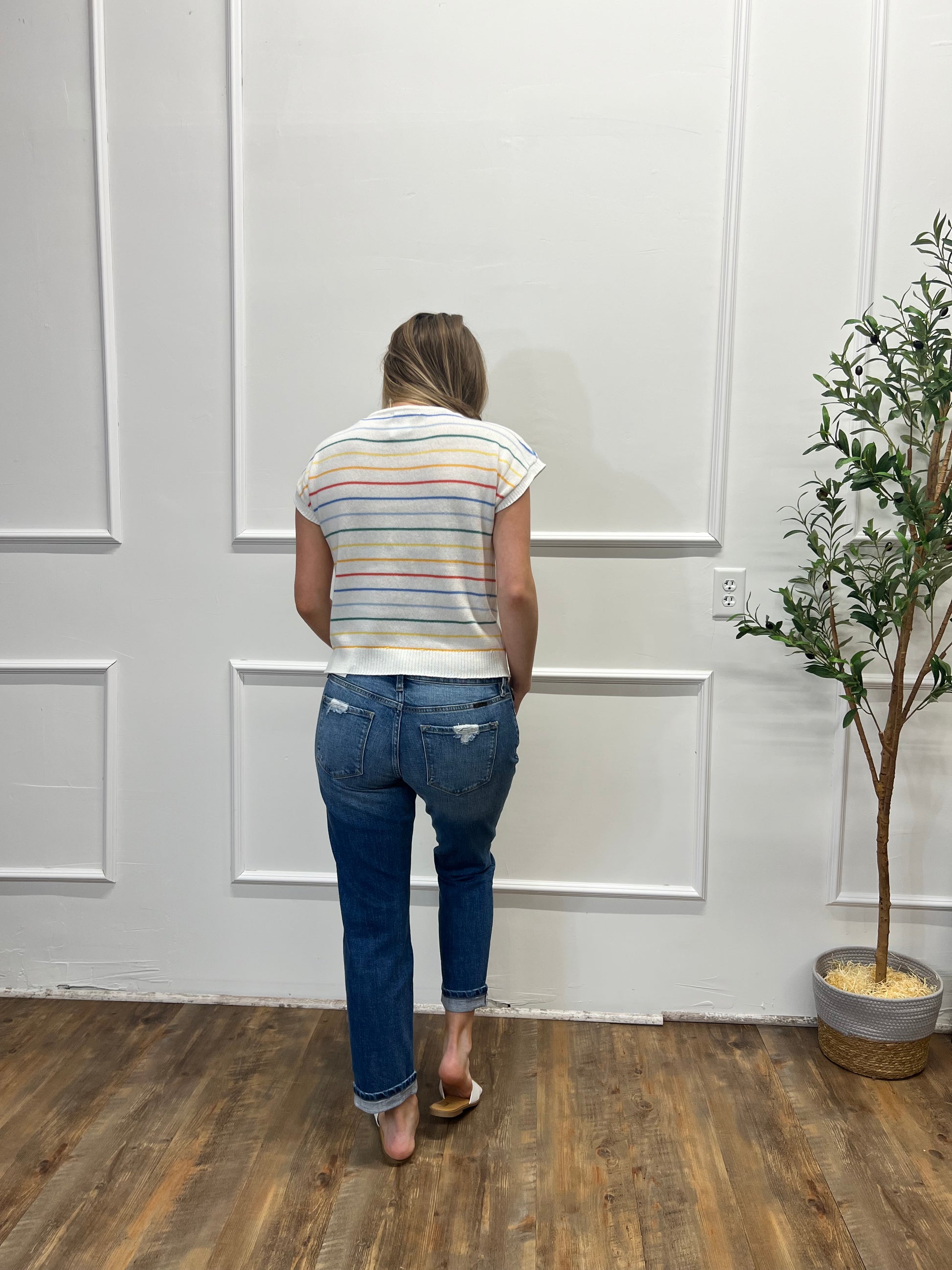 Person wearing a striped shirt and jeans standing in a room with a white door and wooden floor.