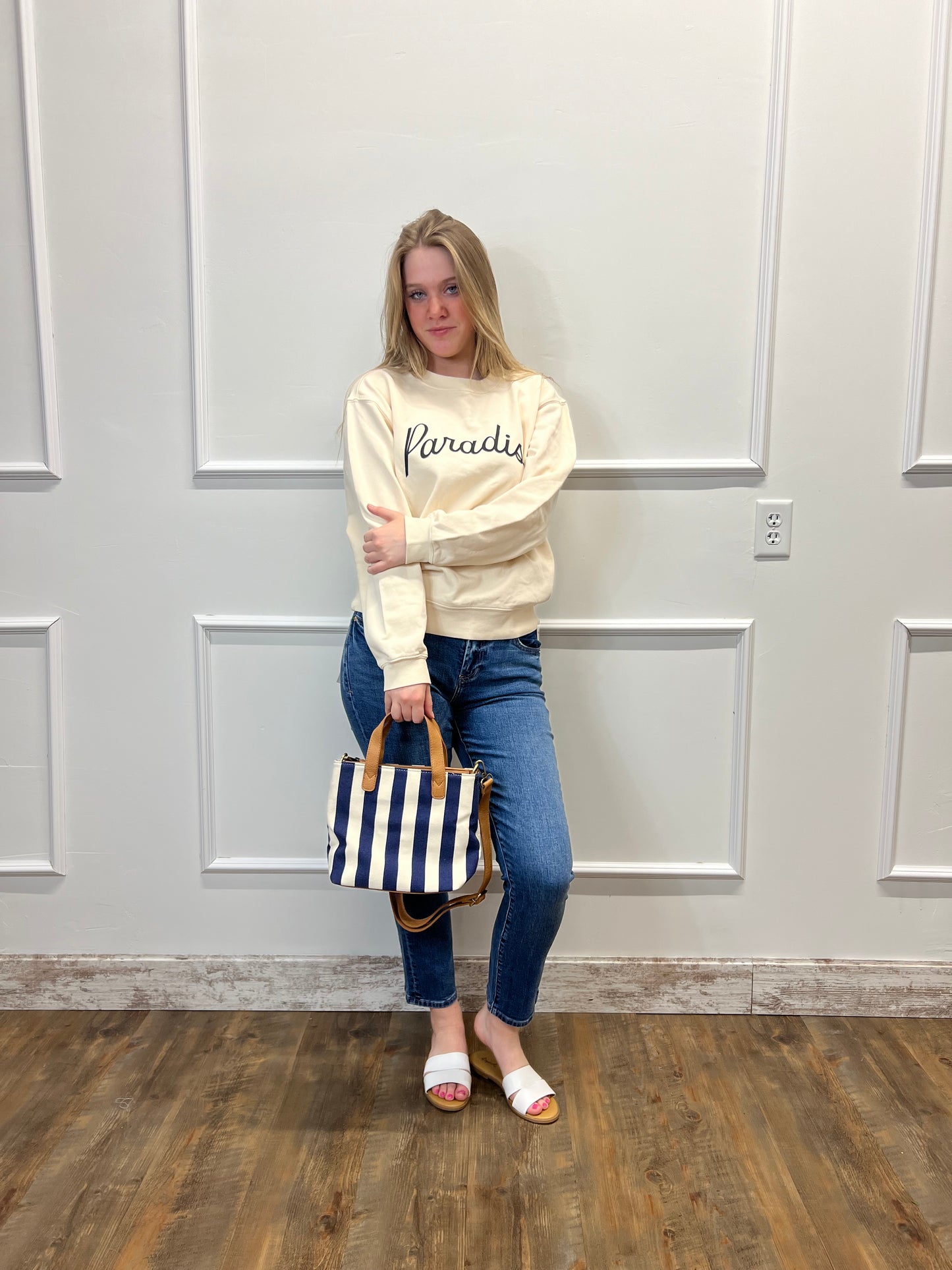 Person wearing a hoodie and jeans standing in front of a white paneled wall.