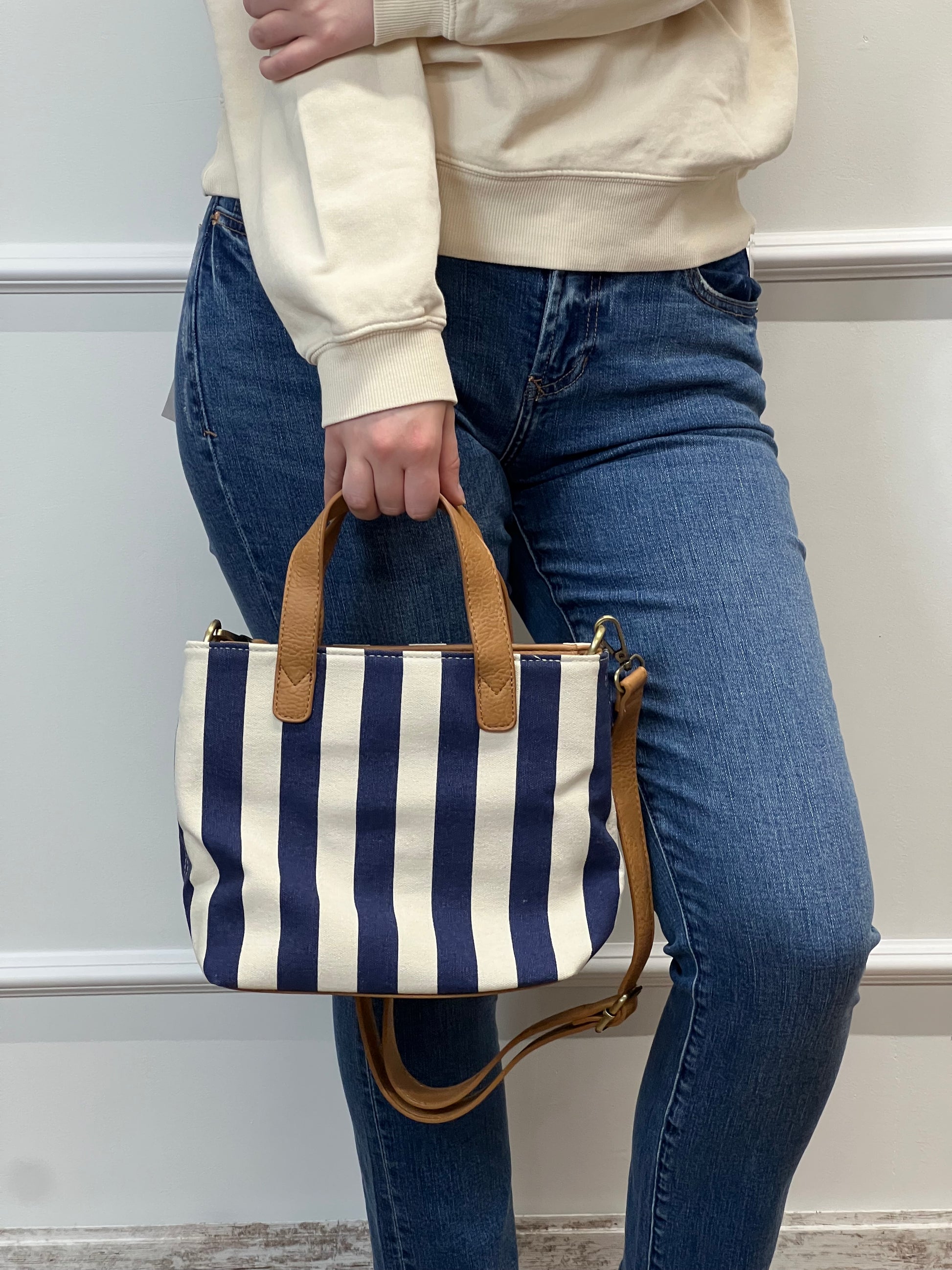 Person holding a navy and white striped bag with a brown handle.