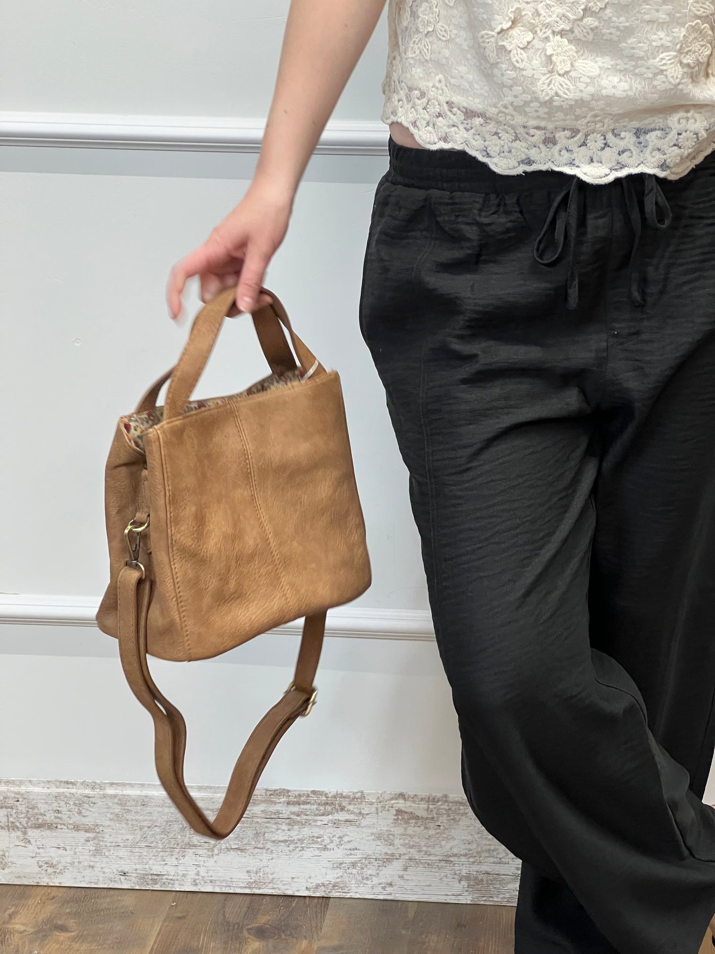 Brown leather bag being held by a hand against a neutral background