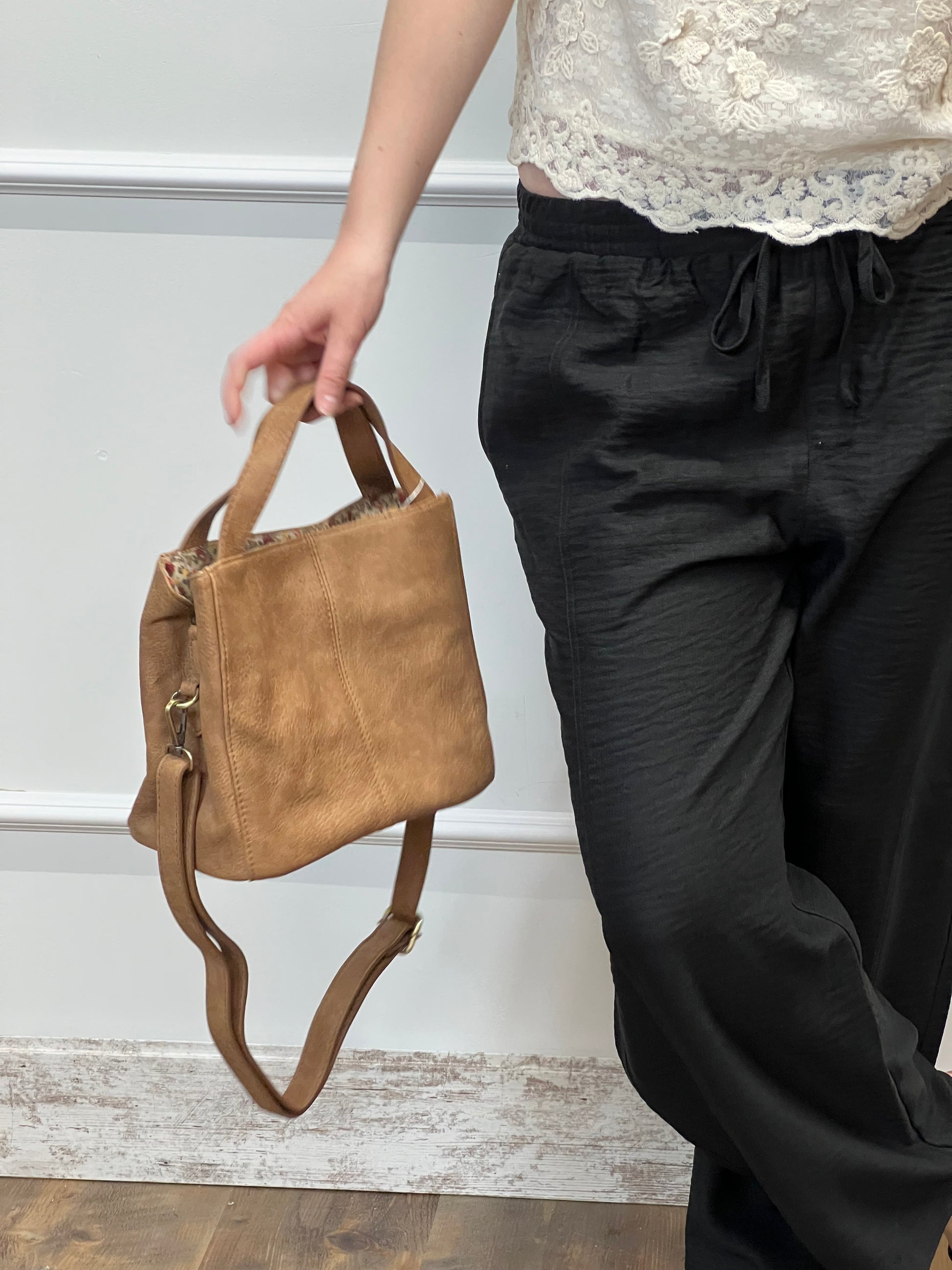 Brown leather bag being held by a hand against a neutral background
