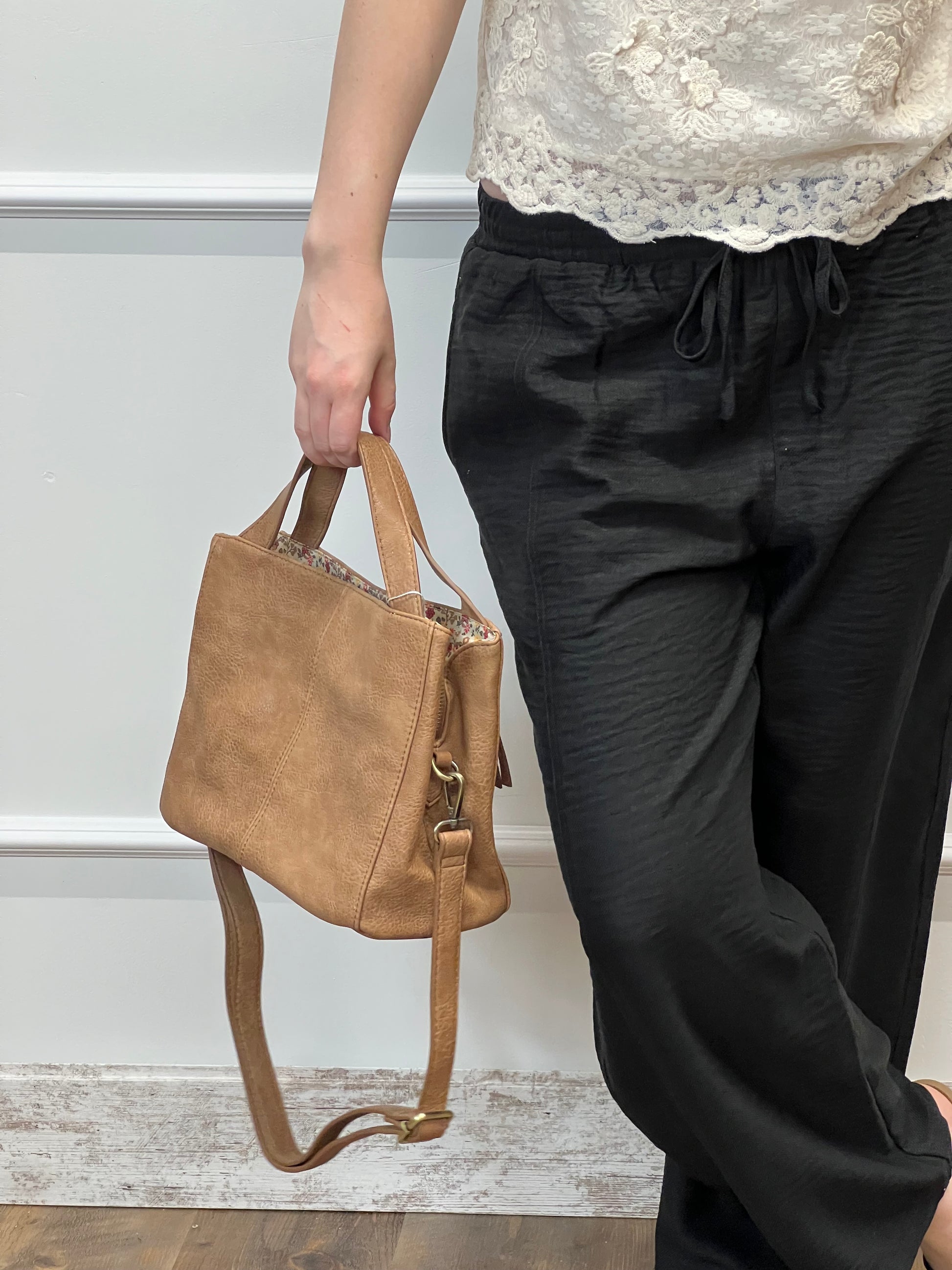 Brown leather bag being held by a person against a neutral background